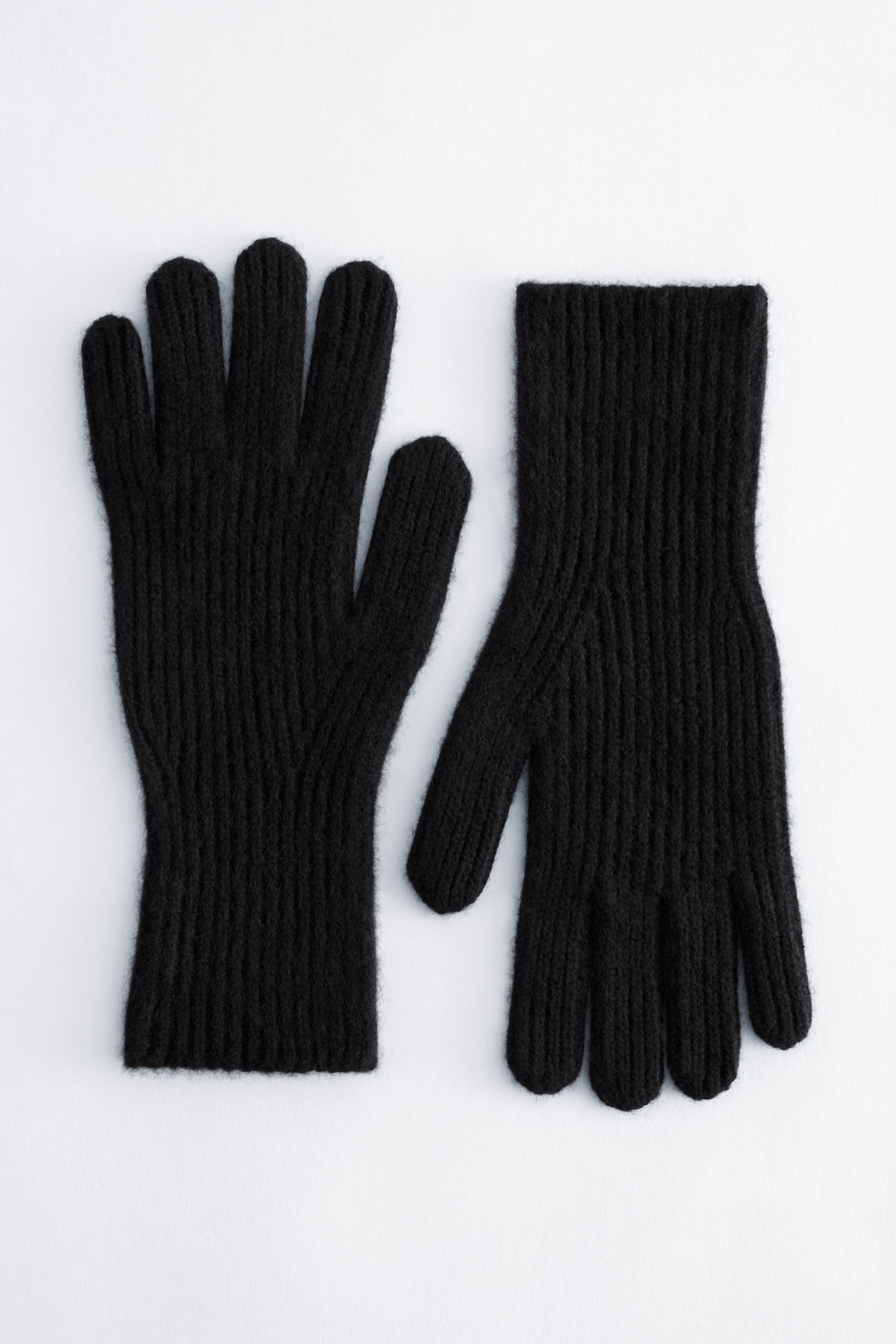 Grotere afbeelding bekijken: Een paar zwarte kasjmieren handschoenen ligt plat, waarbij elke handschoen een geribbelde breistructuur vertoont van de vingertoppen tot aan de boorden.