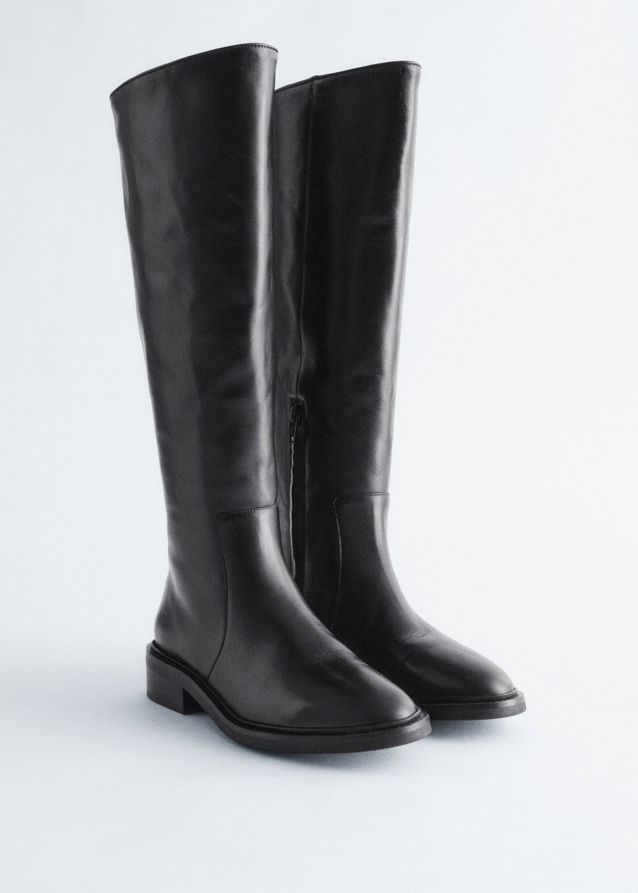 Größeres Bild anzeigen: Ein Paar schwarze Lederreitstiefel wird aus einem frontalen Winkel präsentiert, mit hohen Schäften, niedrigen Blockabsätzen und Gummisohlen. Ein verdeckter Reißverschluss ist entlang der Innenseite des Schafts des rechten Stiefels sichtbar.