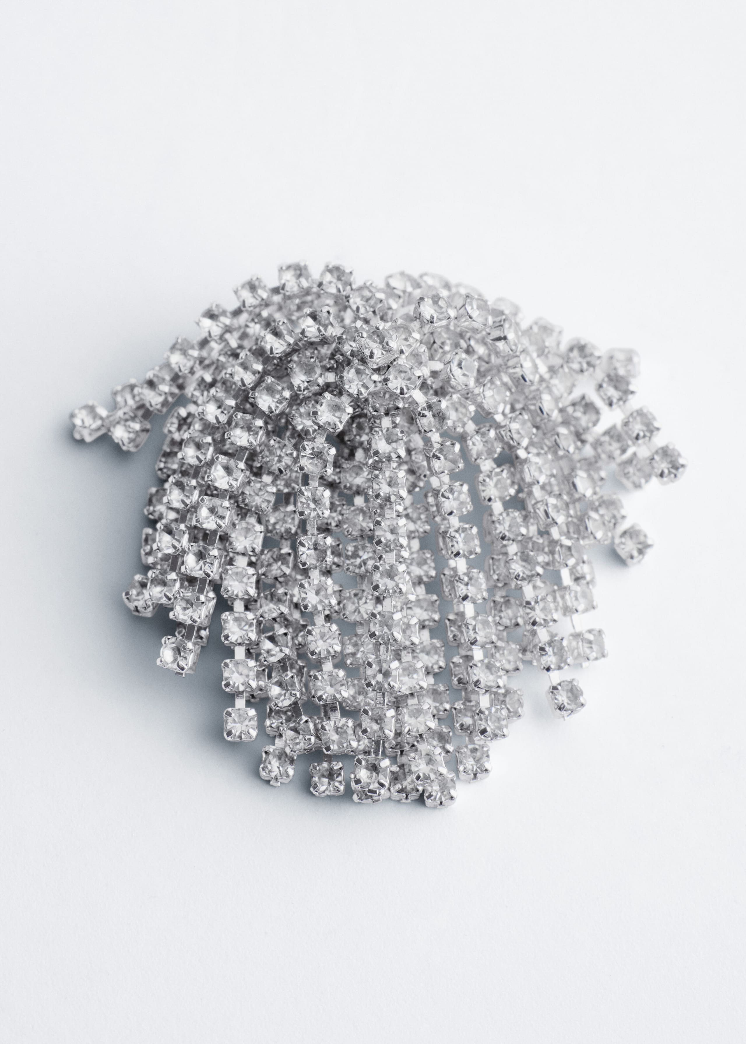 A brass earring showcases a cluster of cascading strands embellished with clear, square-cut rhinestones. The strands drape downward from a domed top to create a shimmering, tiered fringe design.