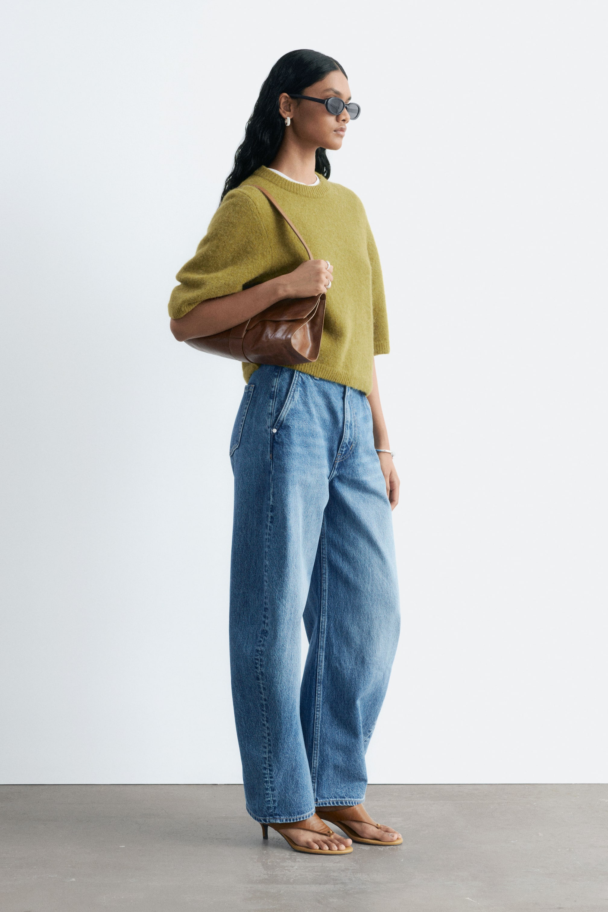 Visa större bild: Avslappnade blå denimjeans med hög midja, böjda barrel-leg-ben och en vintageinspirerad tvätt bärs av modellen. Jeansen är stylade med en grön kortärmad tröja med struktur och bruna sandaler med klack.