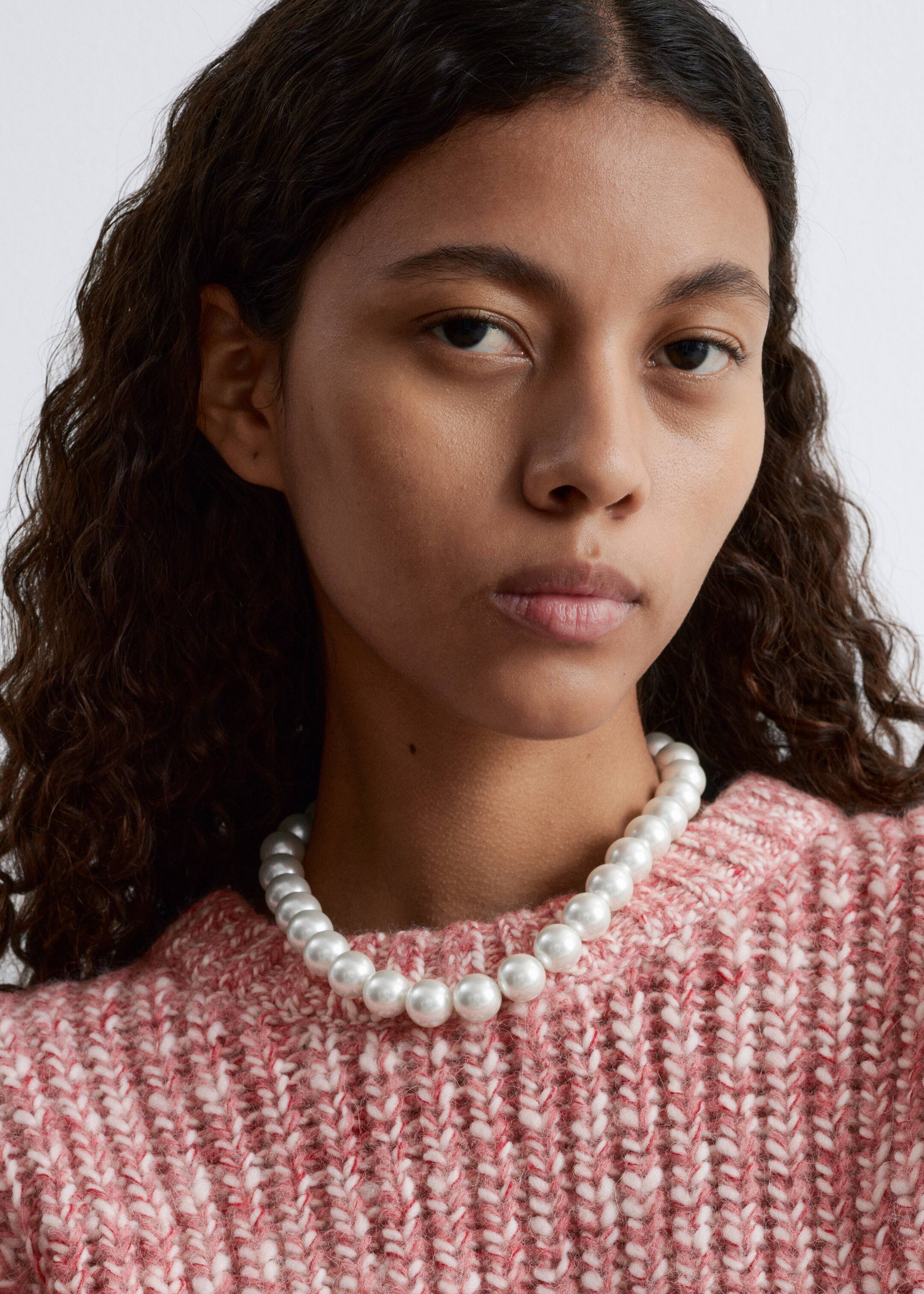 Visa större bild: En pärlhalsband omger halsen, med en enkel rad av jämnstora vita pärlor. Den vilar på en texturerad rosa och vit chunky stickad tröja.