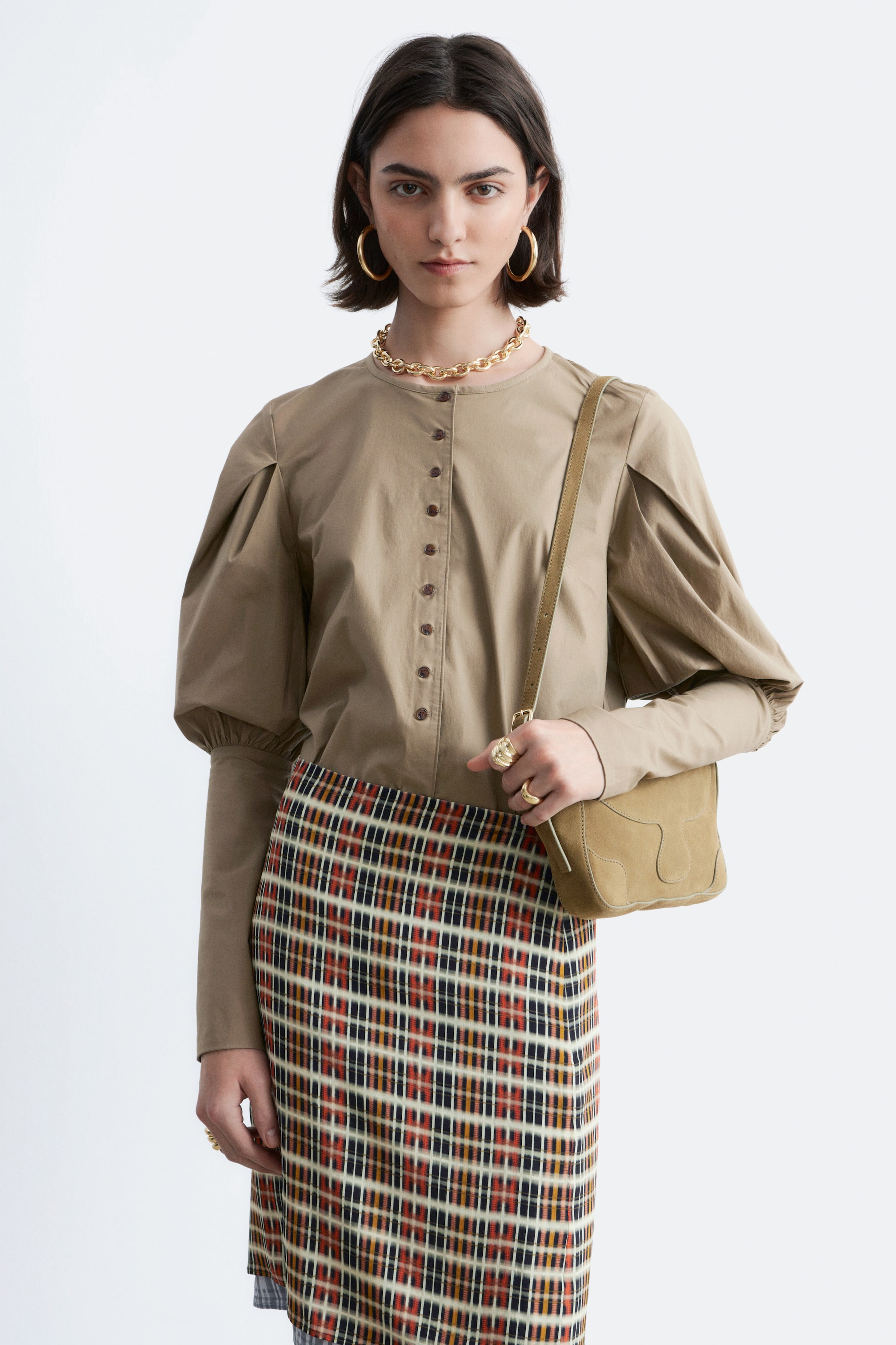 Visualizza immagine più grande: Una blusa beige presenta uno scollo rotondo e un'abbottonatura completa con piccoli bottoni marroni. È progettata con maniche voluminose, raccolte sia sulle spalle che sui polsini.