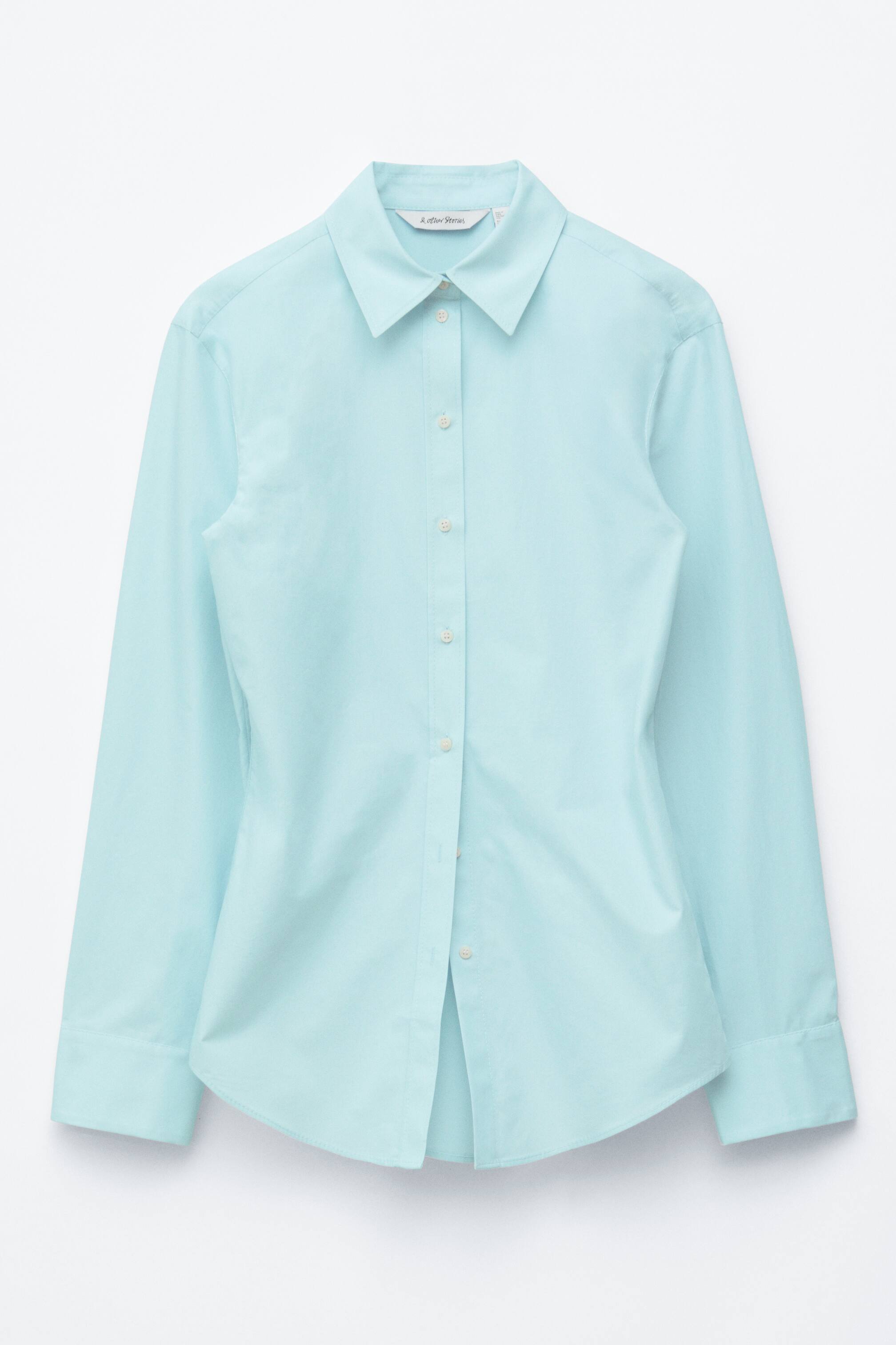 Visualizza immagine più grande: Una camicia azzurra è mostrata frontalmente, caratterizzata da un colletto a punta, un'abbottonatura completa con bottoni chiari e maniche lunghe con polsini abbottonati. La camicia presenta una silhouette affusolata con un orlo curvo e un'etichetta del marchio bianca è visibile sul retro interno del colletto.