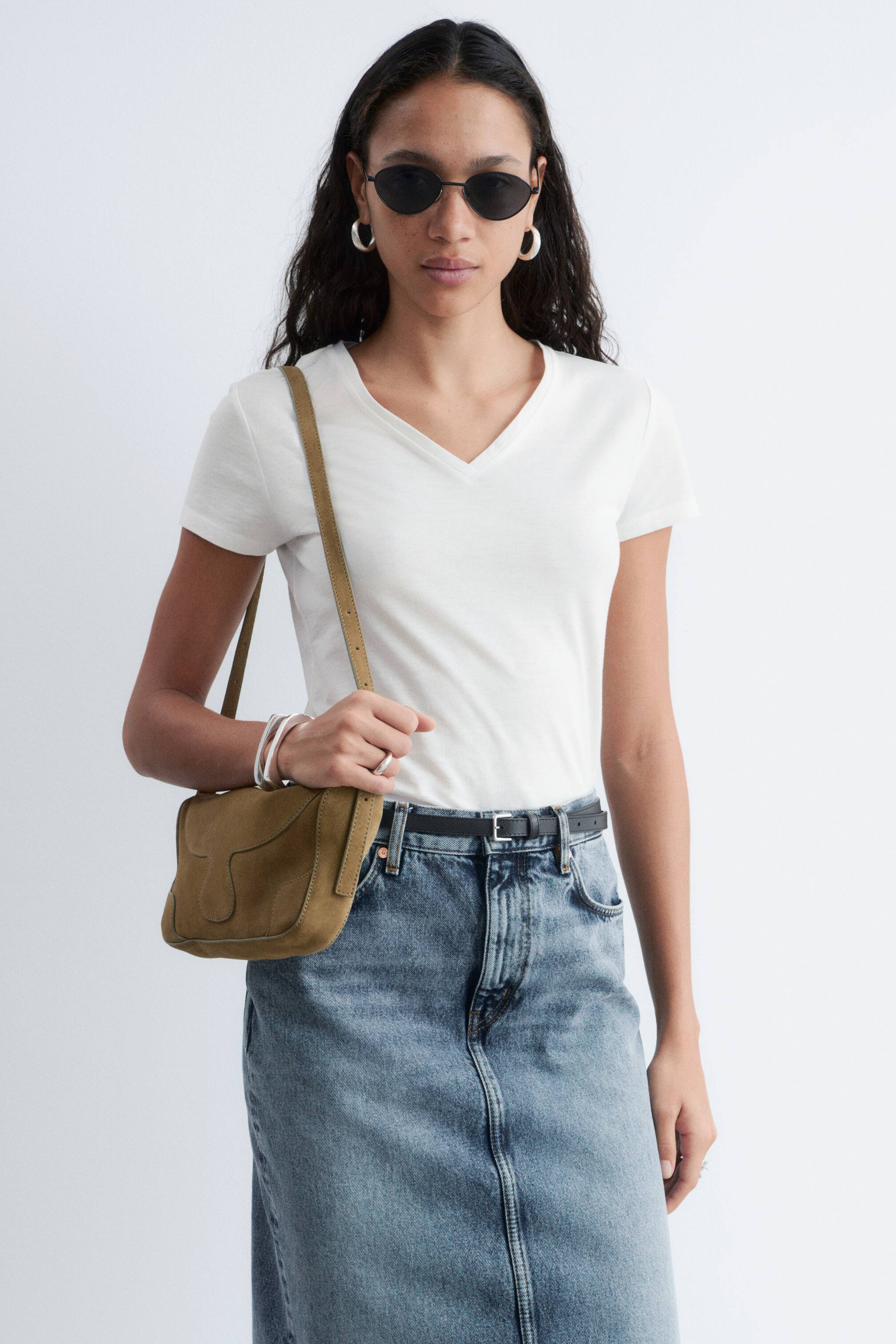 Grotere afbeelding bekijken: Een wit t-shirt met v-hals heeft korte mouwen en een v-halslijn, en sluit nauw aan op de romp. Het wordt gedragen in een blauwe denim rok.