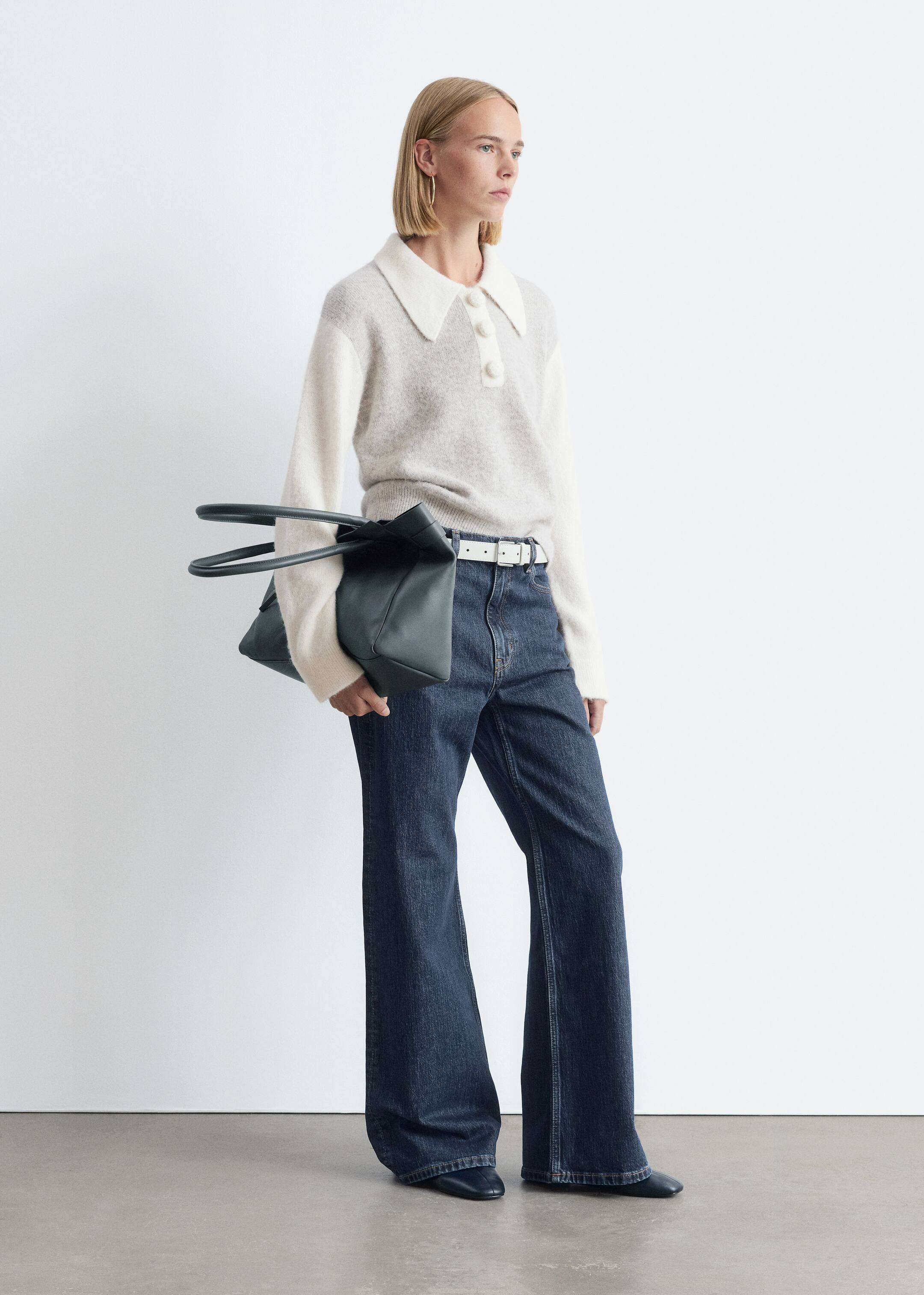 Ver imagen más grande: Un jersey de punto, con un cuerpo gris claro, mangas largas blancas con puños acanalados y un cuello blanco extragrande con una tapeta de tres botones, está siendo usado por la modelo. La modelo también lleva unos vaqueros de lavado oscuro y un cinturón blanco, y sostiene un bolso tote verde oscuro.