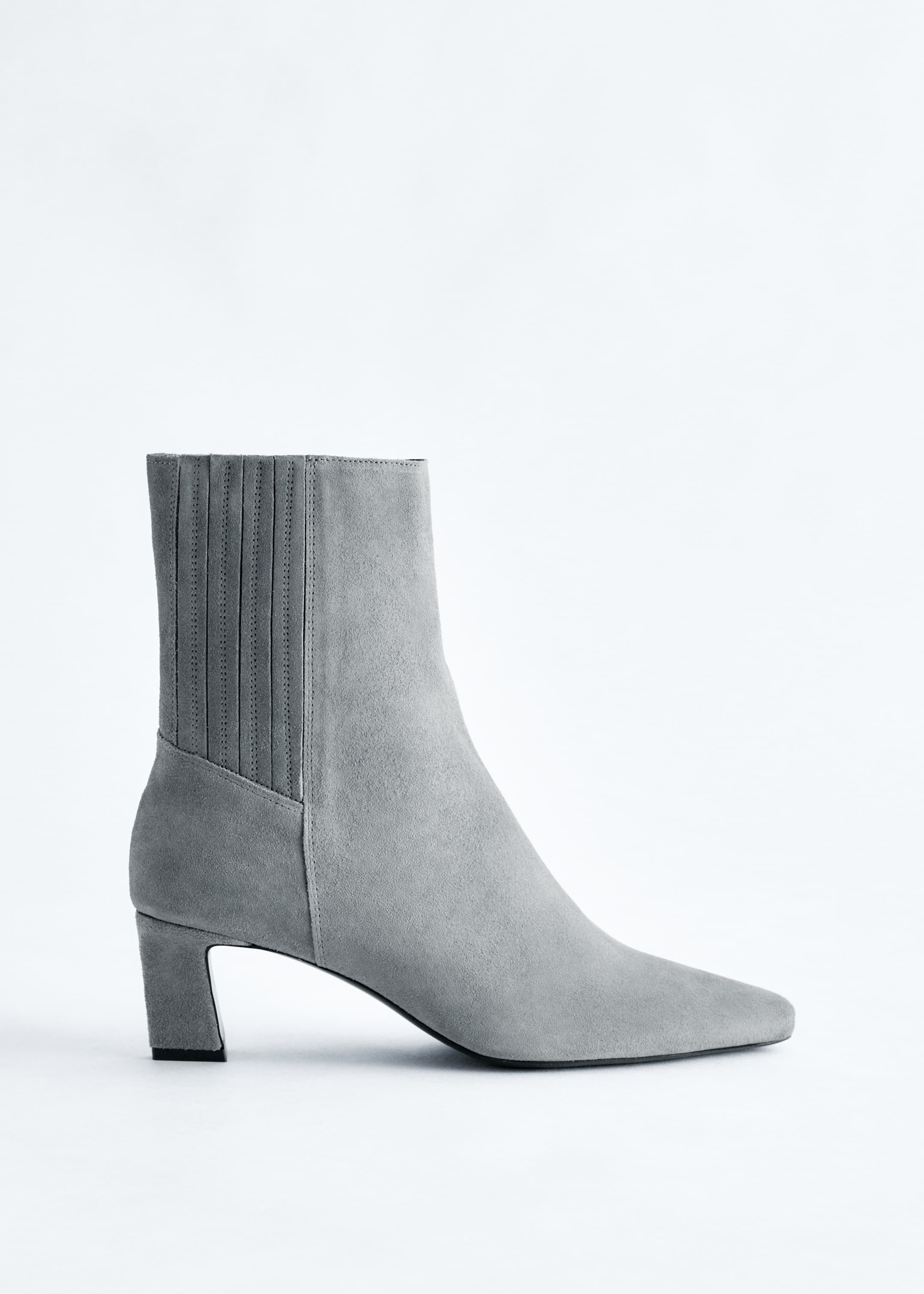 View larger image: A grey suede ankle boot is facing left, displaying a distinctive pointed toe and a neat kitten heel. The ankle shaft is featuring vertical pleats on its inner side.
