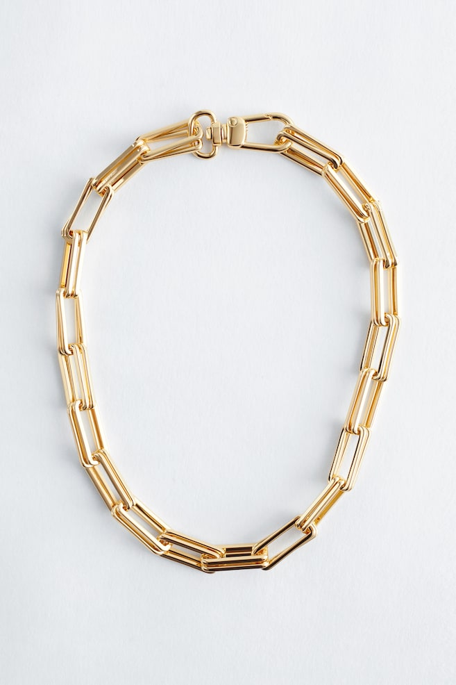 Un collier à maillons épais de couleur or est présenté de face, formant une forme circulaire courte, et comportant des maillons rectangulaires allongés avec une fermeture à fermoir pivotant. - 1