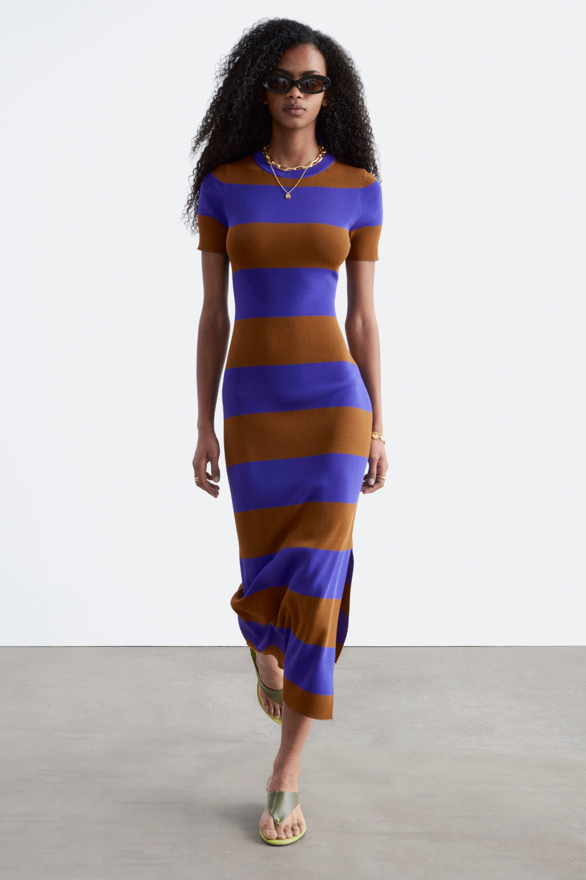 Größeres Bild ansehen: Ein Midikleid mit abwechselnden horizontalen Streifen in warmem Braun und lebhaftem Blau-Violett. Es ist mit kurzen Ärmeln und einem runden Halsausschnitt geschnitten und präsentiert eine figurbetonte Silhouette mit einem seitlichen Schlitz nahe dem Saum.