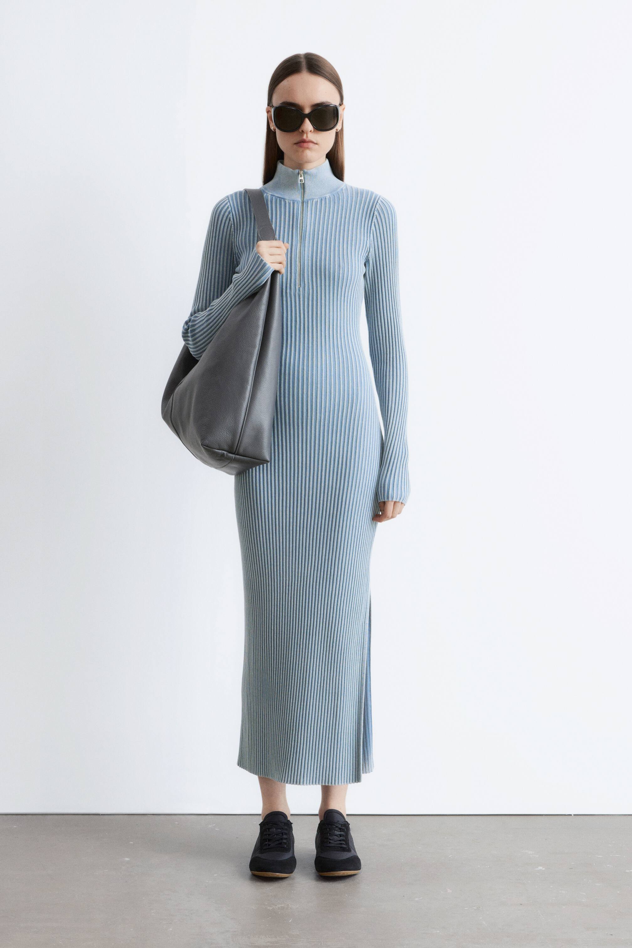 Преглед на по-голямо изображение: Светлосиня, рипсена плетена, прилепнала макси рокля е представена отпред. Характеризира се с висока яка с предно закопчаване с цип, дълги ръкави и страничен разрез на левия крак.