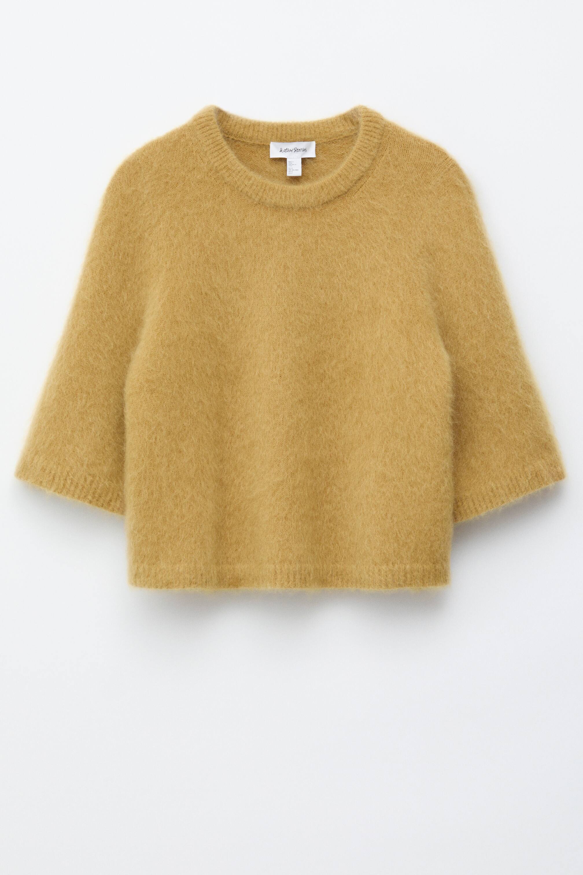 הצגת תמונה גדולה יותר: חולצת הטריקו הסרוגה בצבע צהוב זהב מוצגת מהחזית, ומציגה מרקם מוברש ומטושטש וסילואטה רפויה. היא מעוצבת עם קו צוואר עגול, גימורים מצולעים בקו הצוואר, בשוליים ובחפתים, ושרוולים שמסתיימים מעט מעל המרפקים.