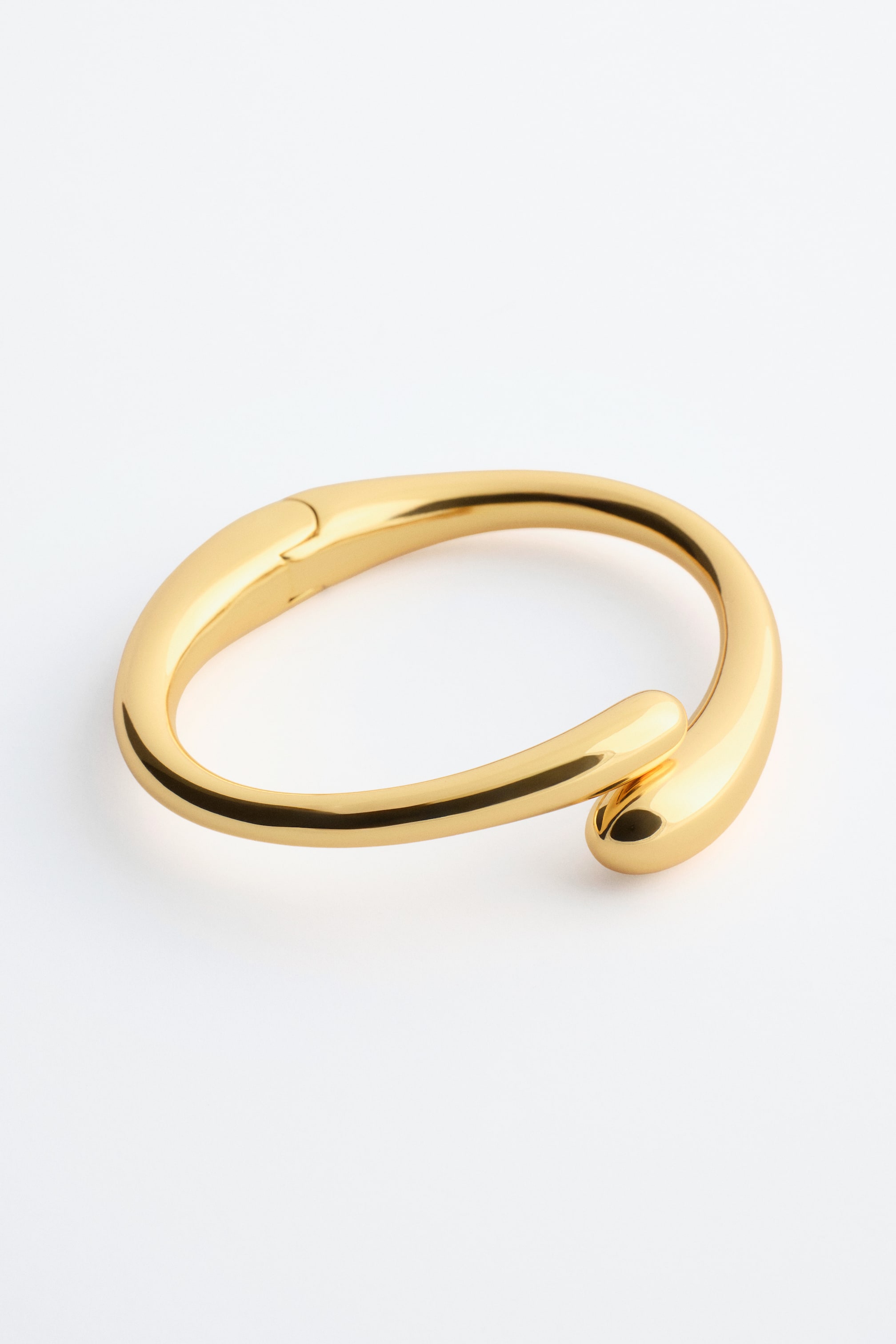 Visa större bild: En skulptural manschettarmband i polerad zink med flytande linjer, vars ändar gradvis breddas. Det har ett gångjärnsstängning på ena sidan.
