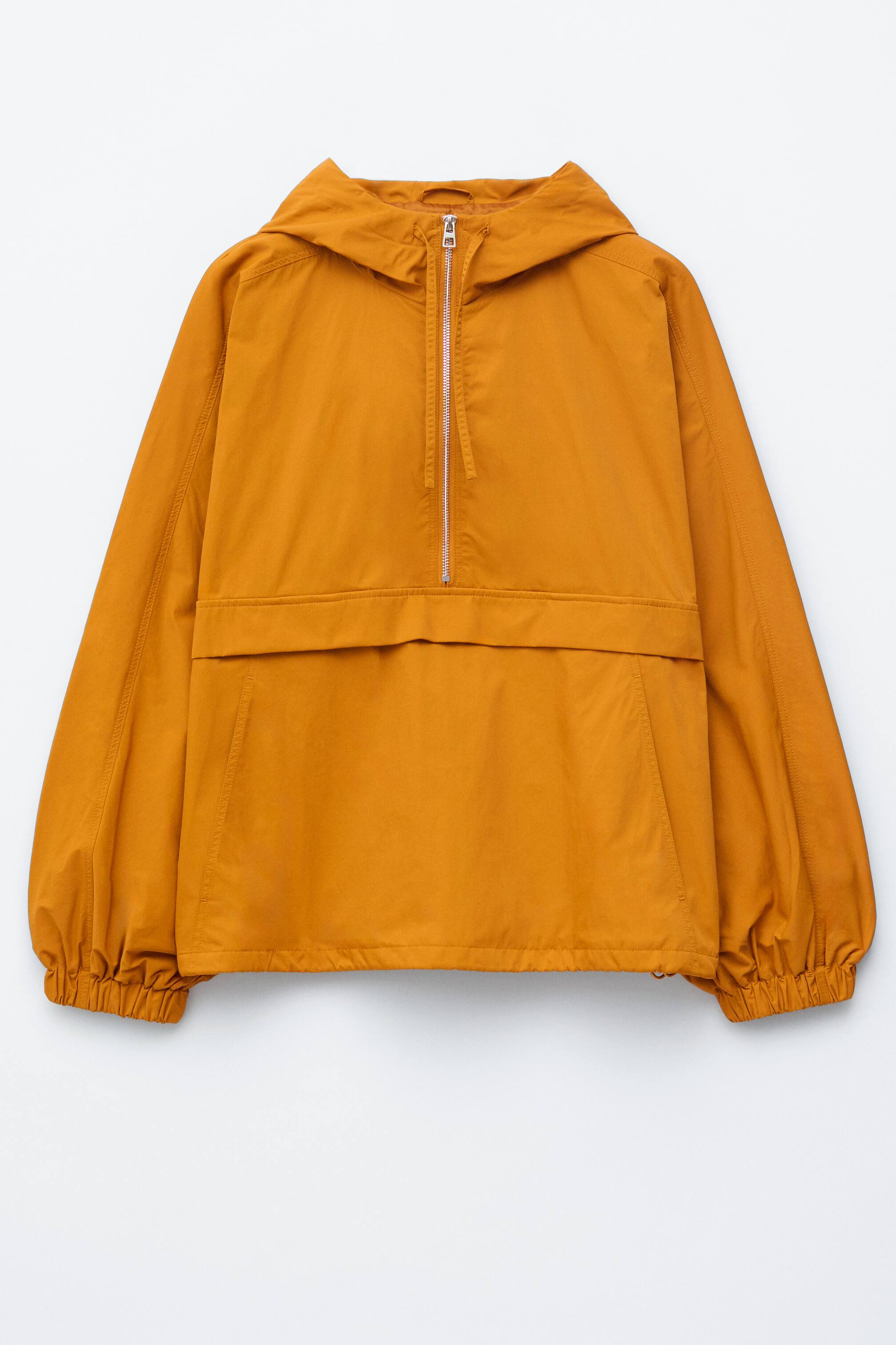 Ver imagem maior: Um anoraque frontal ocre apresenta um capuz incorporado, um fecho de correr prateado de um quarto com detalhe de cordão, um grande bolso frontal com aba horizontal e punhos e bainha elásticos.