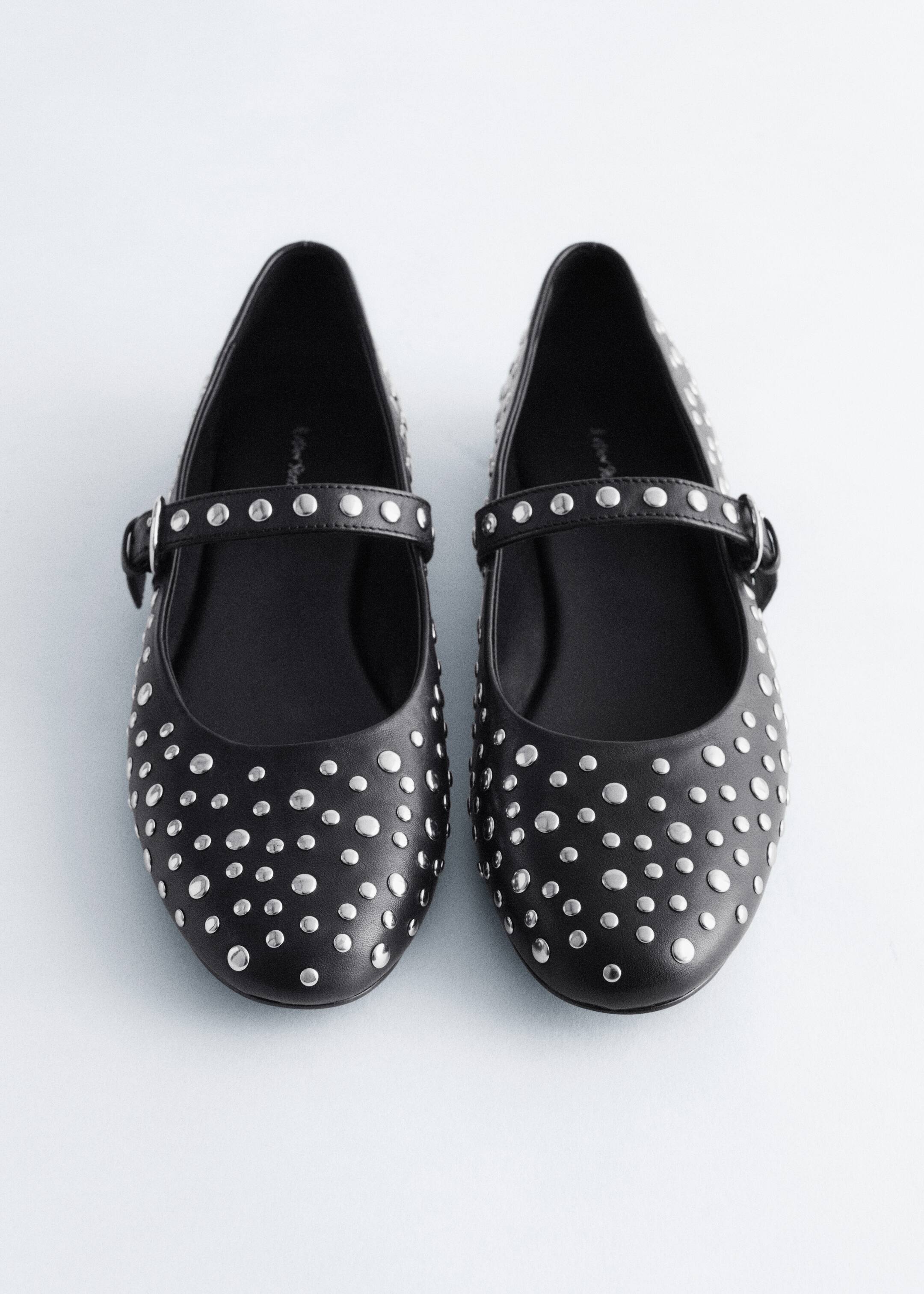 View larger image: A pair of black leather Mary Jane ballet flats is being presented from the front. Each flat is featuring allover silver-toned metal studs and a strap across the vamp that is secured by a tonal black buckle.