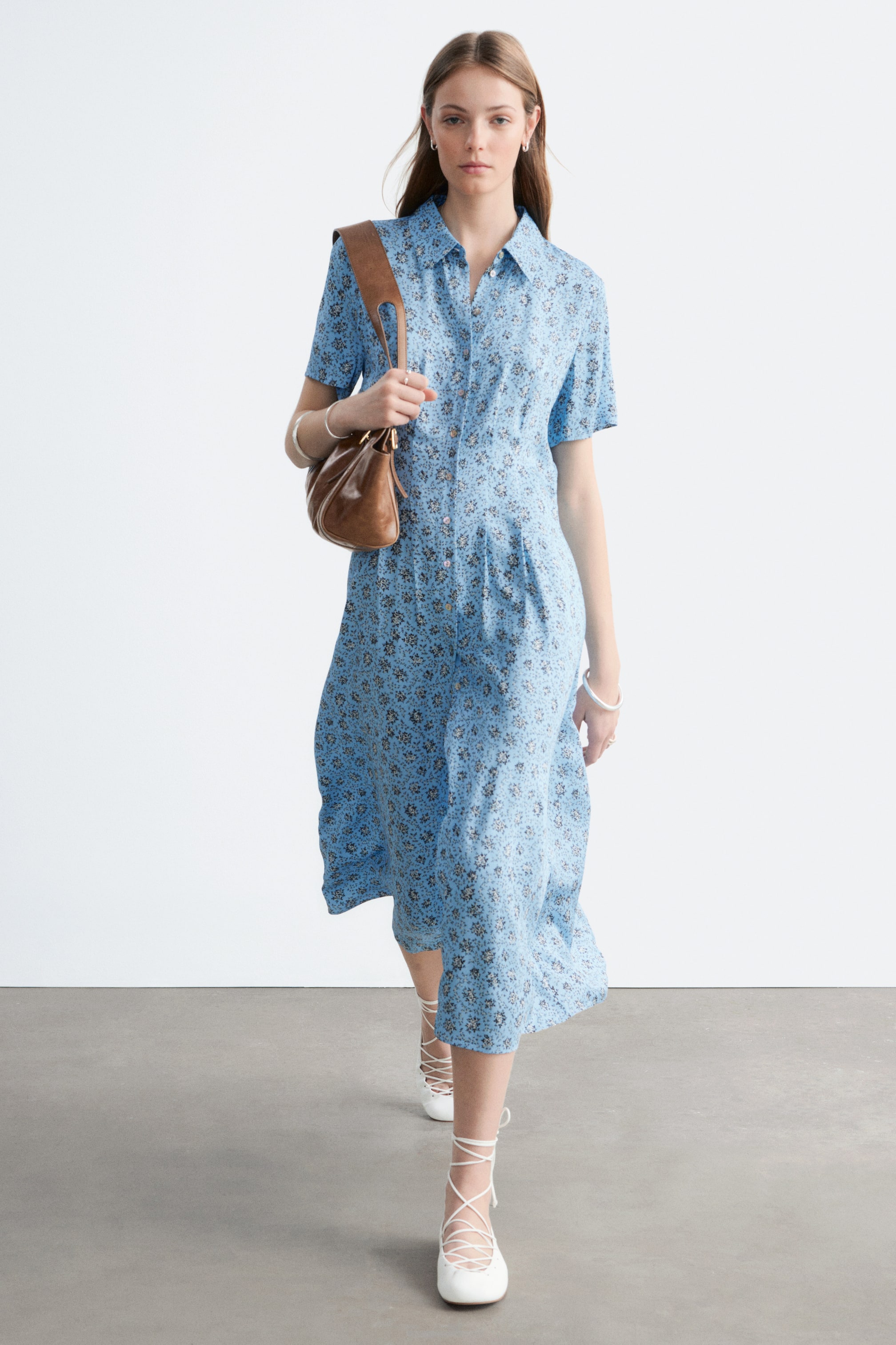 Zobacz większy obraz: Jasnoniebieska sukienka koszulowa z kwiatowym wzorem posiada spiczasty kołnierzyk, krótkie rękawy i zapięcie na guziki z przodu. Została zaprojektowana z marszczonym pasem i opada do długości midi, prezentowana z lekko ukośnego widoku z przodu.