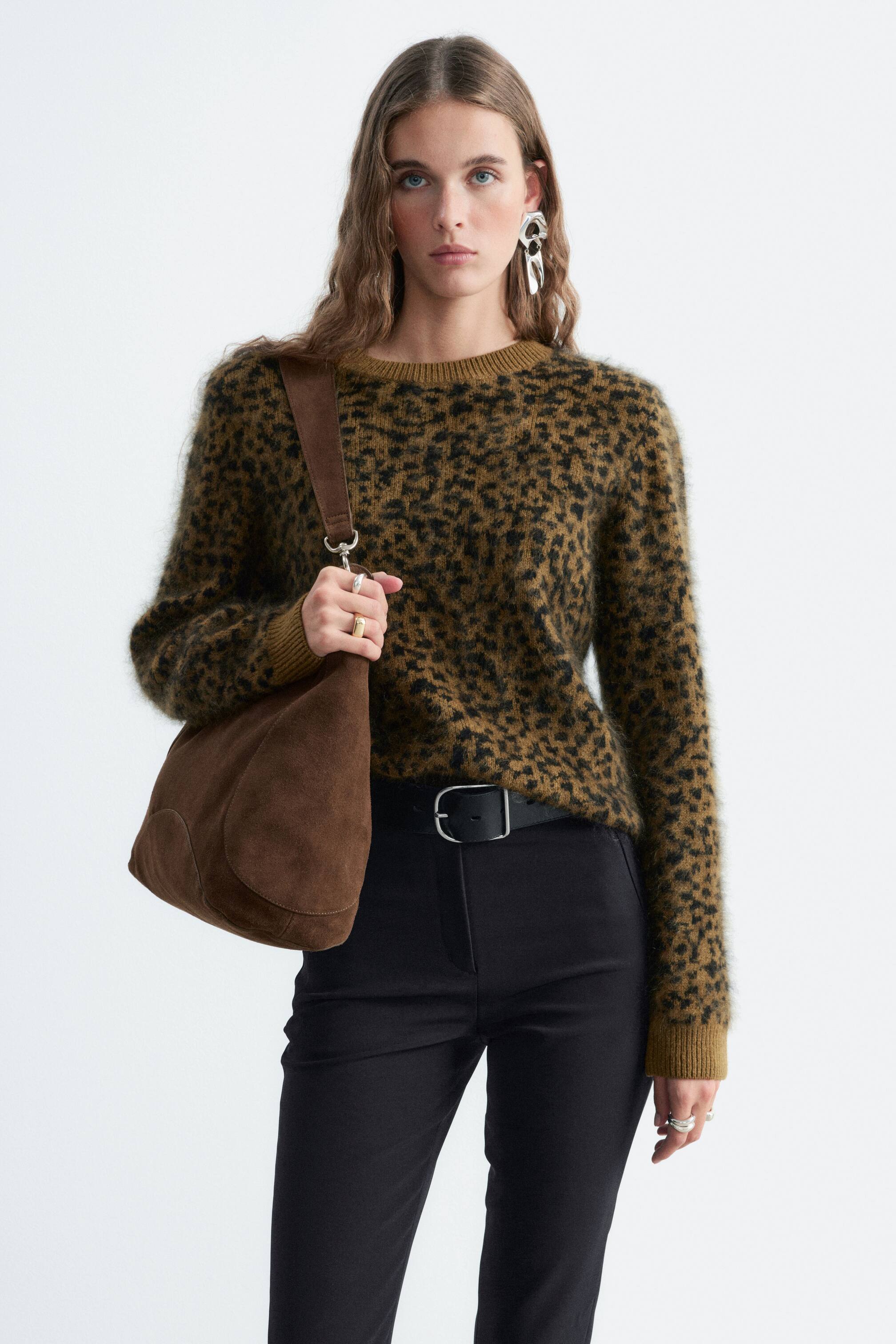 Vezi imaginea mai mare: Un pulover din lână merinos, cu un tricot pufos, texturat și imprimeu leopard maro și negru, este purtat de model. Puloverul cu decolteu rotund este stilizat cu pantaloni negri și o geantă de umăr din piele întoarsă maro, purtată pe umăr.
