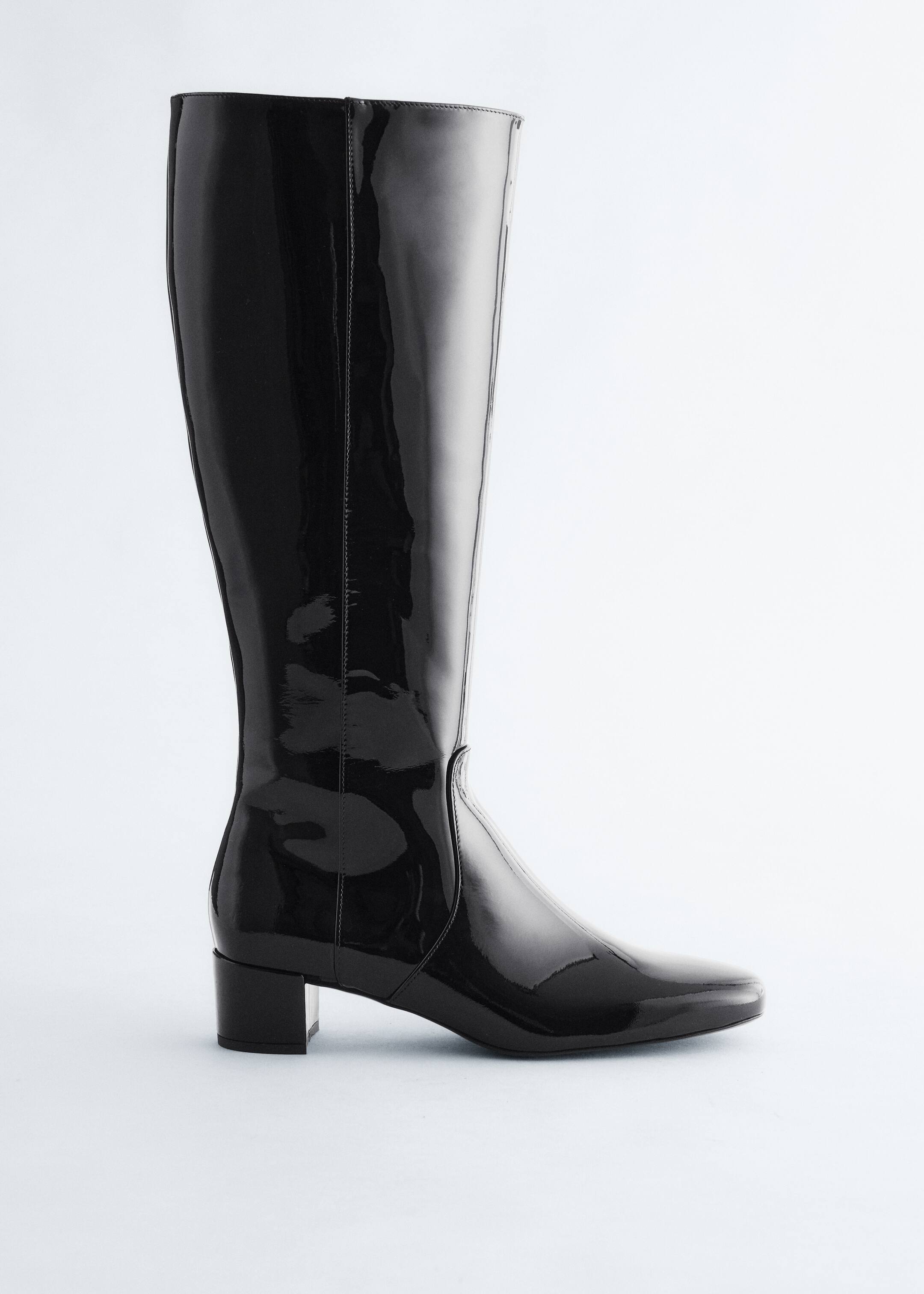Agrandir l'image: Une botte noire à hauteur de genou est inclinée vers la gauche, avec une finition en cuir verni brillant. Elle est conçue avec une tige haute et ajustée, un bout en amande et un talon bloc bas.