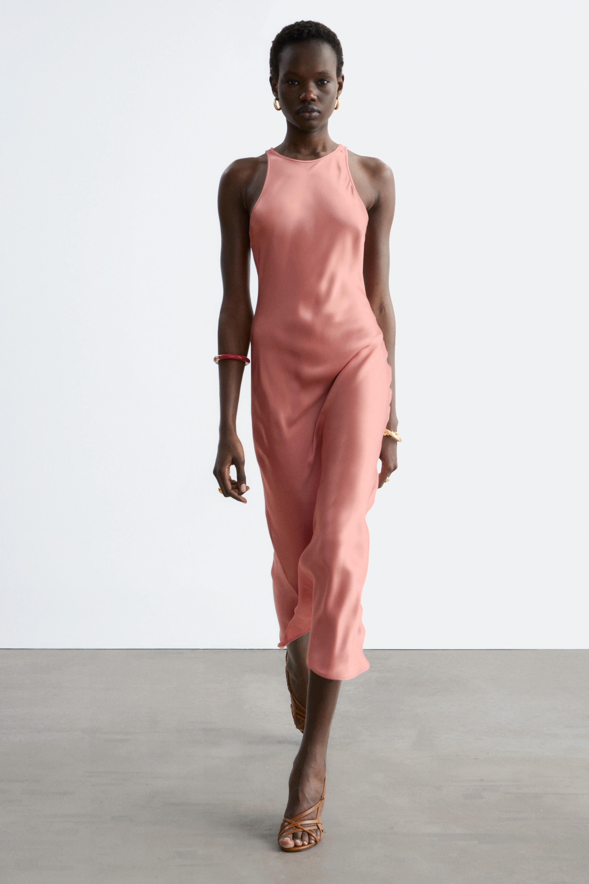 Visualizza immagine più grande: Un abito sottoveste in raso color corallo viene presentato, caratterizzato da uno scollo alto arrotondato e sottili spalline, che si drappeggia fino a una lunghezza midi.