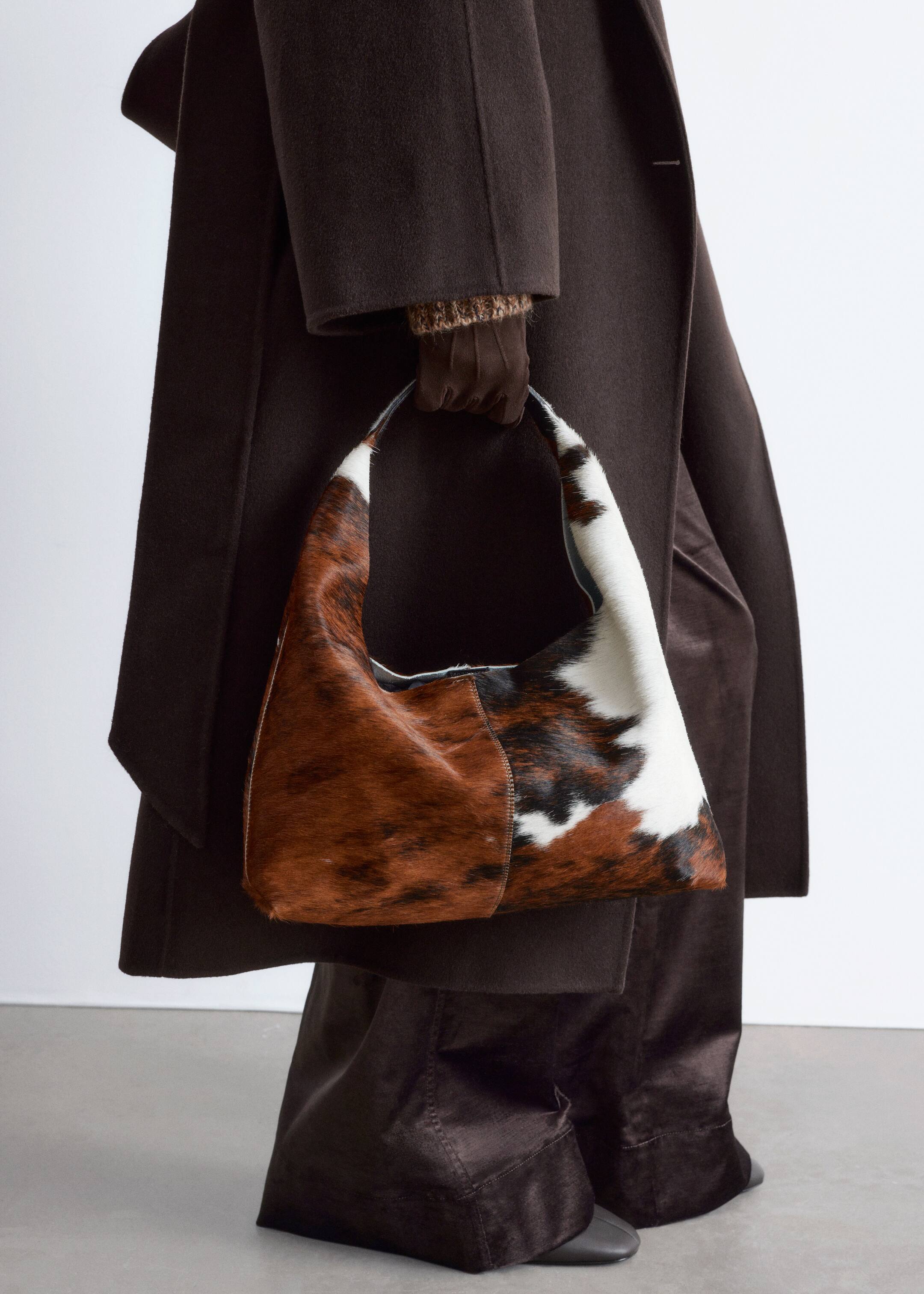 Agrandir l'image: Un sac à main hobo décontracté est tenu par sa sangle, offrant une vue de face. Il arbore un motif en peau de vache dans des nuances de brun-rouge, de noir et de blanc.