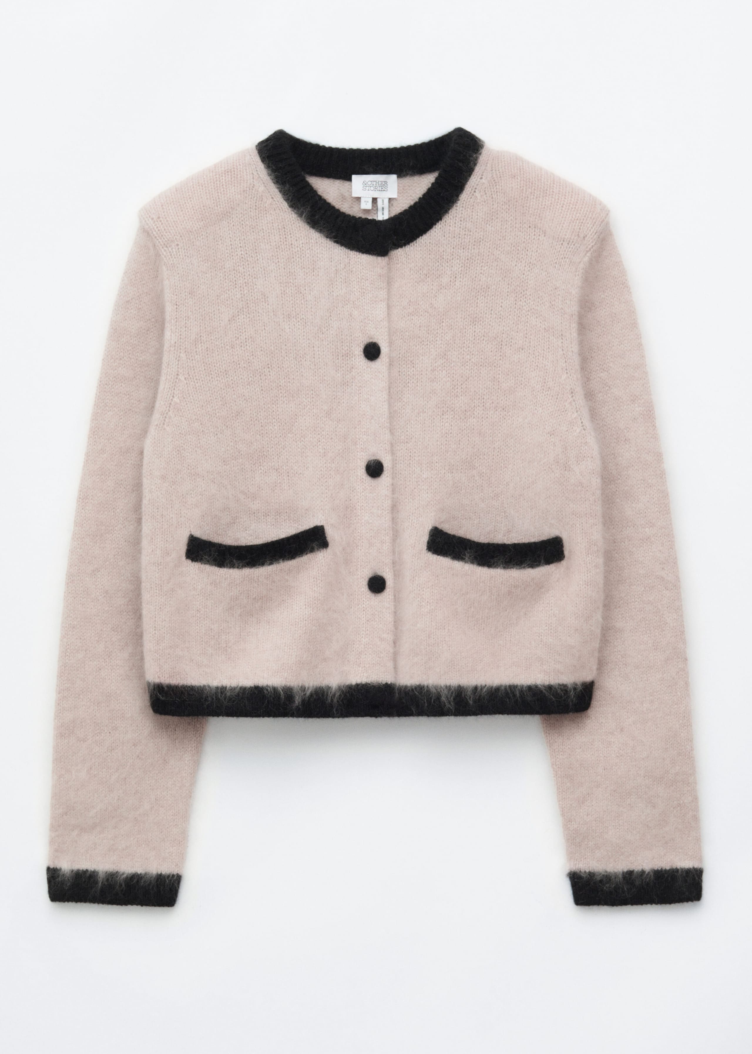 A light beige, fuzzy knit cardigan is shown in a structured front-facing silhouette with padded shoulders. It features a contrasting black ribbed crew neck, matching black cuffs and hem, three black fabric-covered buttons, and two black front pocket trims.