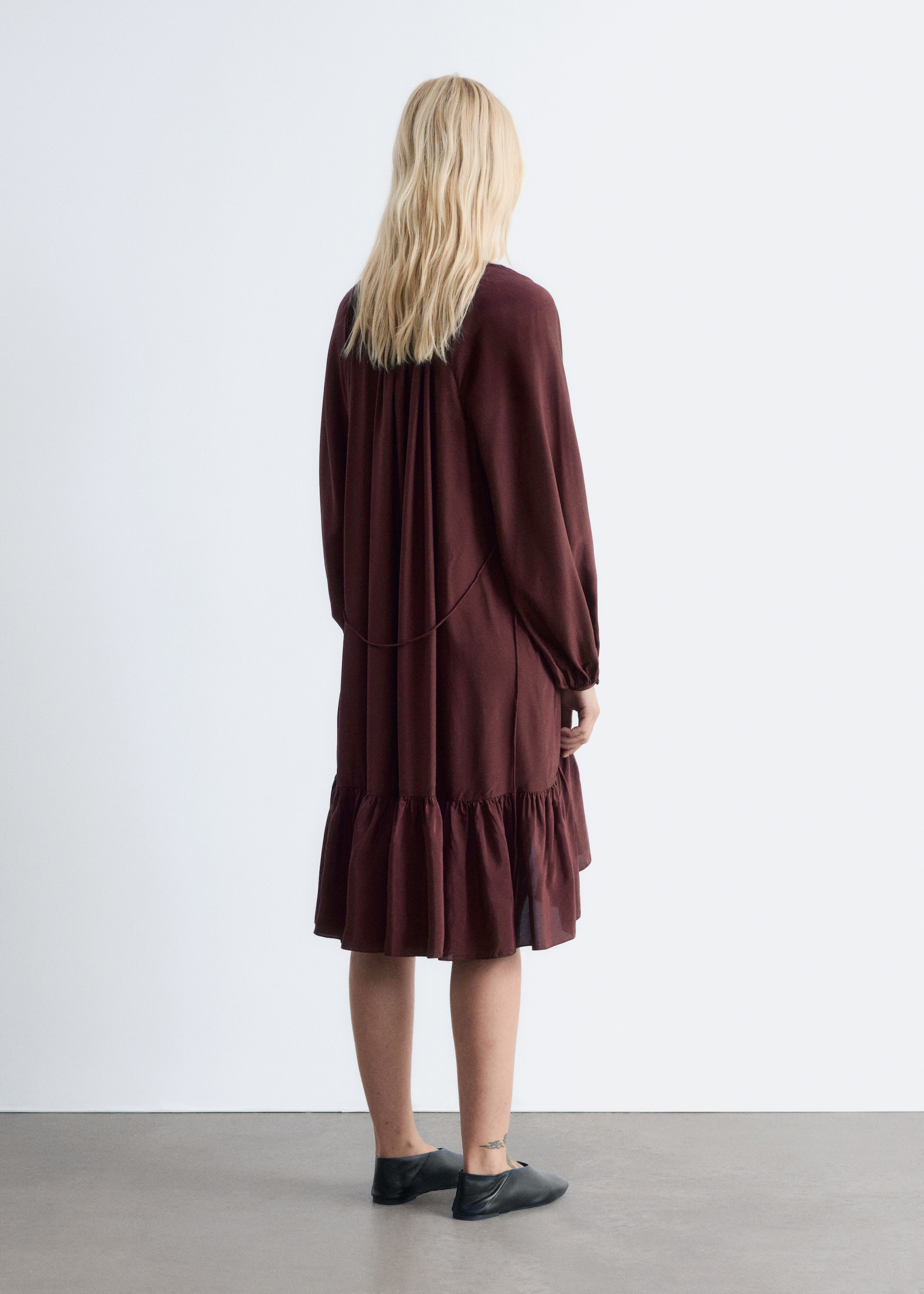 Grösseres Bild ansehen: Ein dunkelrotbraunes Kleid wird von hinten betrachtet, es hat eine lockere Passform mit einem gerafften oberen Rückenpanel, langen Ärmeln mit gerafften Manschetten und einem horizontalen Band über den Rücken. Der gestufte Rock enthält eine breite Rüsche nahe dem mittellangen Saum.