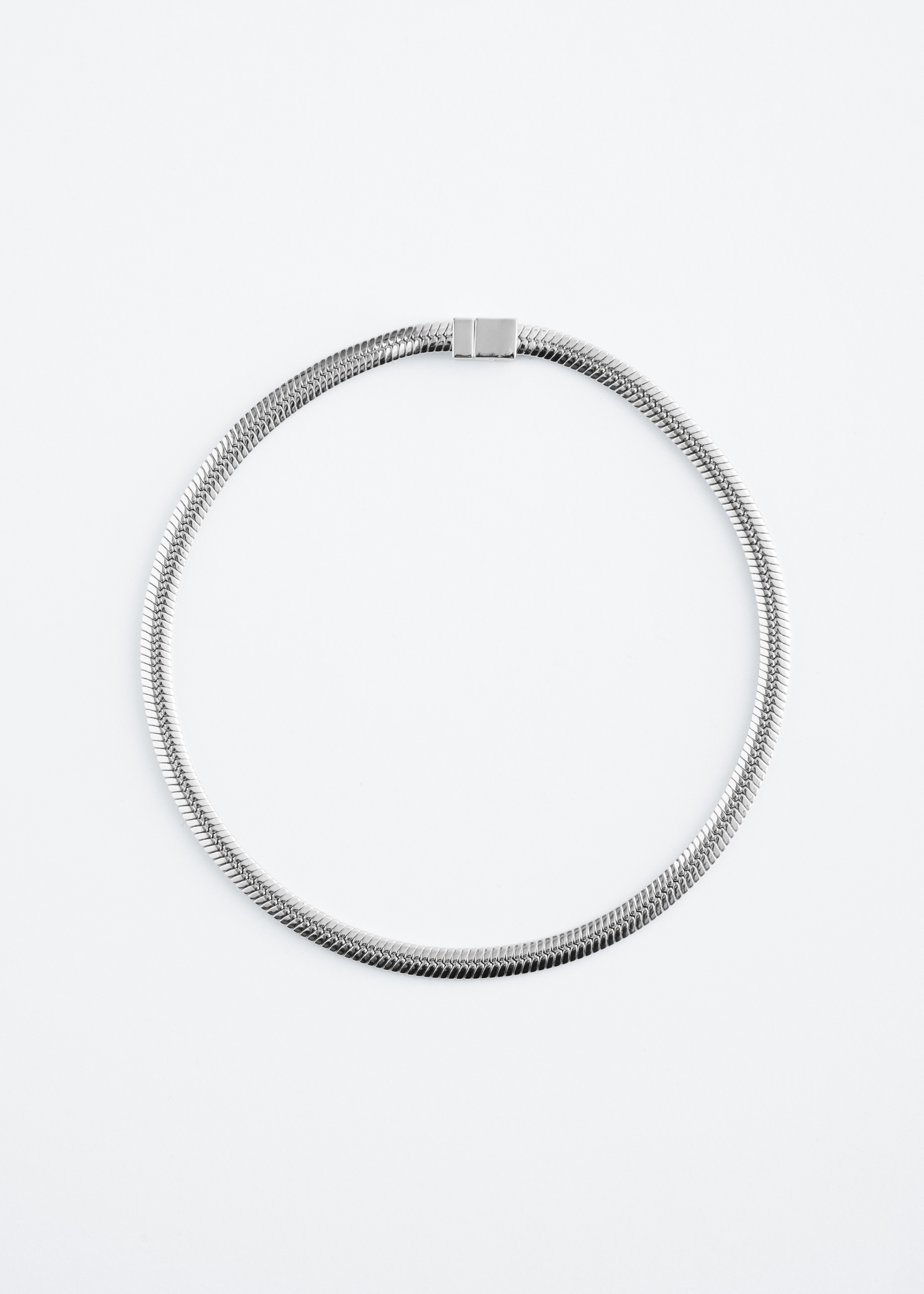 A silver-toned herringbone chain necklace curves elegantly around the neck, resting on a light blue round-neck sleeveless top.