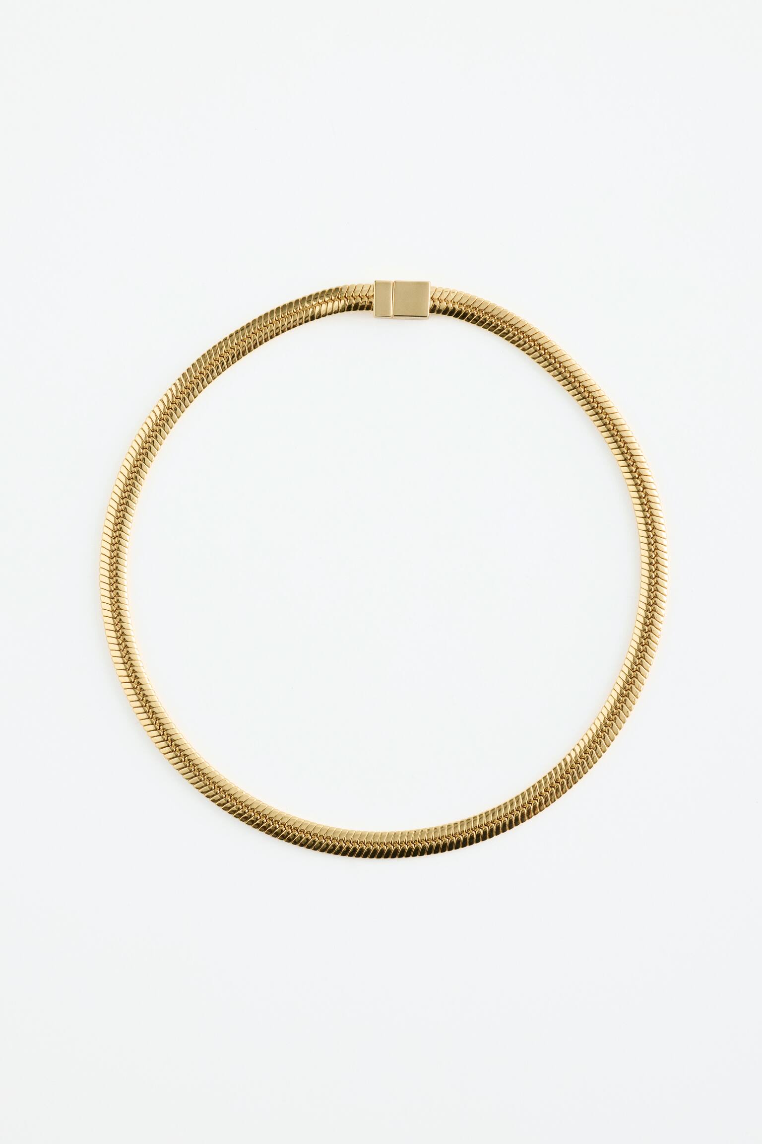 Una cadena de eslabones de espiga dorada yace plana, formando una forma circular. Presenta un cierre rectangular plano en la parte superior. - 1