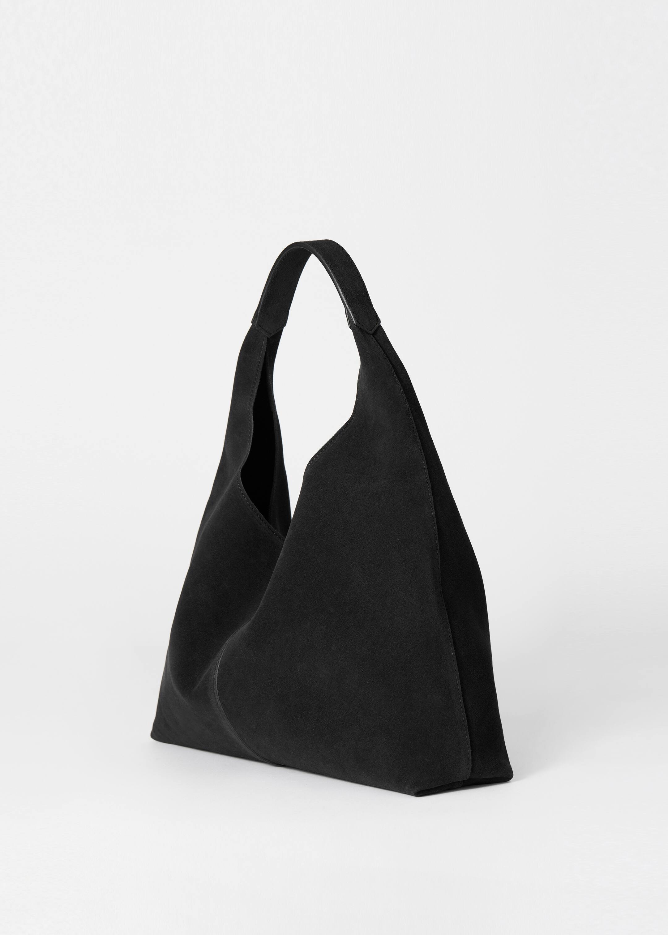 View larger image: A black tote bag is positioned angled to the right, displaying its soft, matte suede material. It is featuring a single wide handle and a decorative vertical seam centered on its front panel.