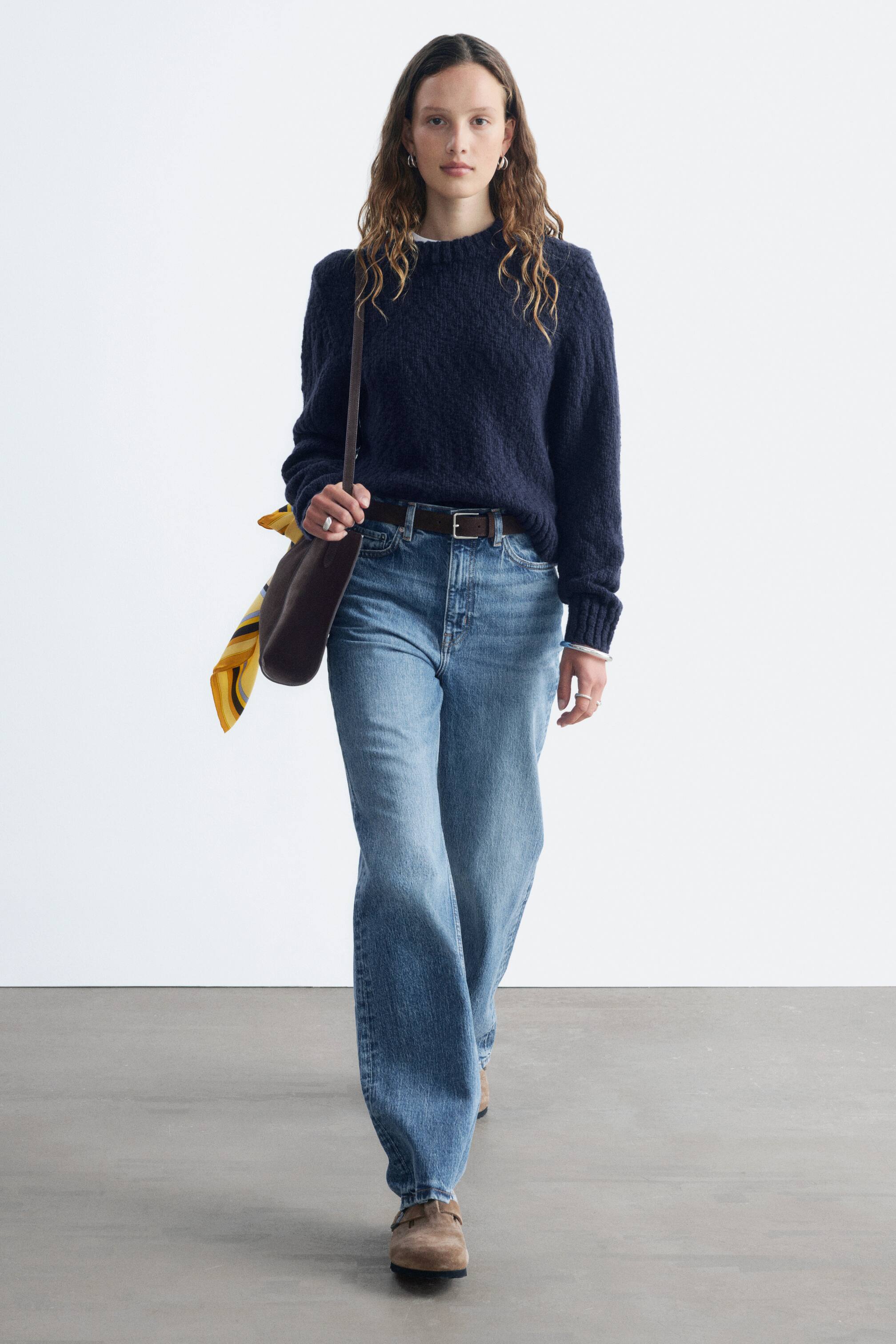 View larger image: The model is wearing a dark blue textured bouclé knit jumper with ribbed cuffs. A white undershirt is visible at the jumper's round neckline and cuffs.