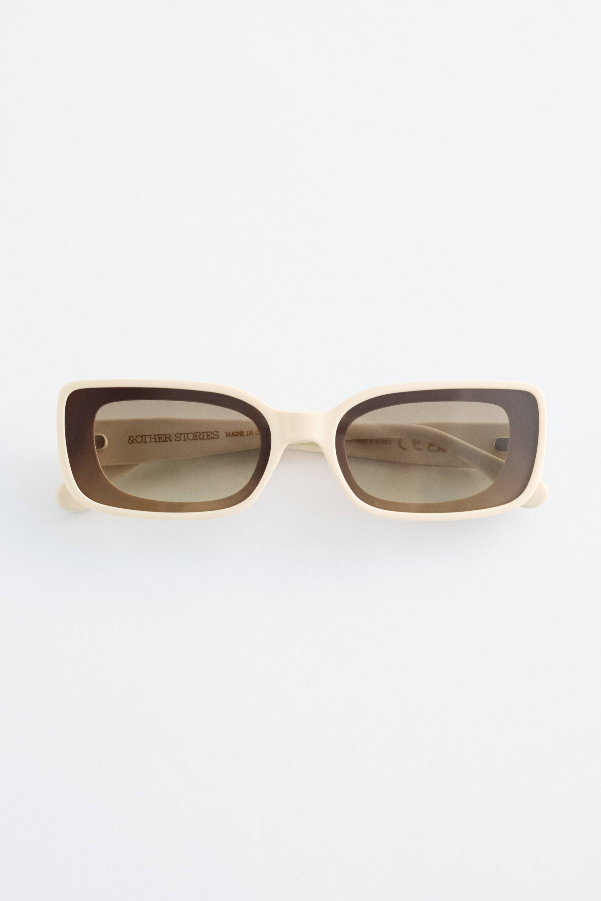 Преглед на по-голямо изображение: Слънчевите очила се отличават с широки правоъгълни рамки с двуцветен дизайн, представящ светъл крем по външните ръбове и тъмно кафяво около затъмнените лещи, и широки дръжки, които съответстват на светлия крем рамка.