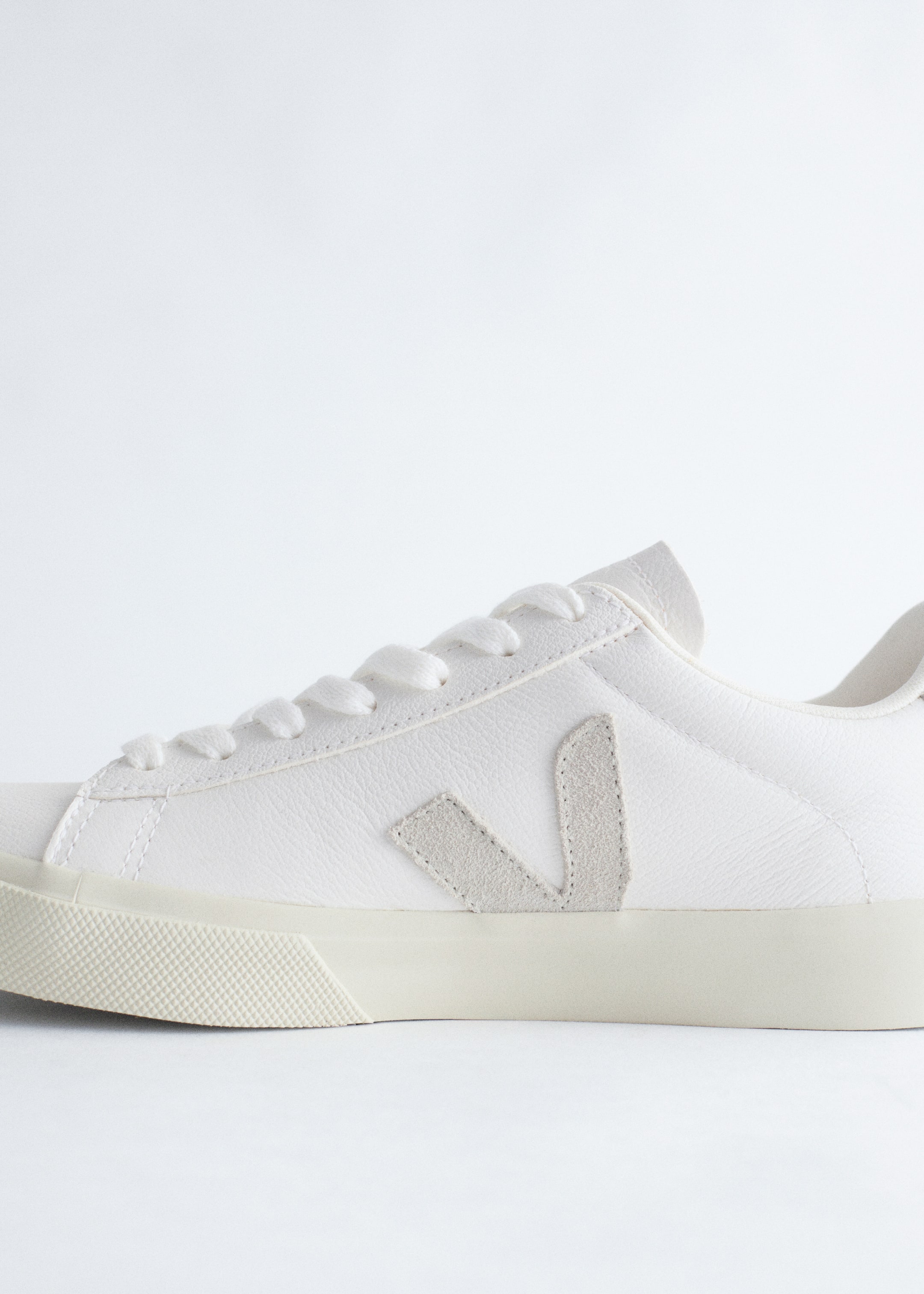 Ver imagen más grande: Una zapatilla Veja 'Campo' se presenta mirando hacia la derecha, con una parte superior de cuero texturizado blanco y cordones blancos. Muestra un logotipo 'V' de gamuza de color más claro en el lateral y una suela de goma en color blanco roto que contrasta.