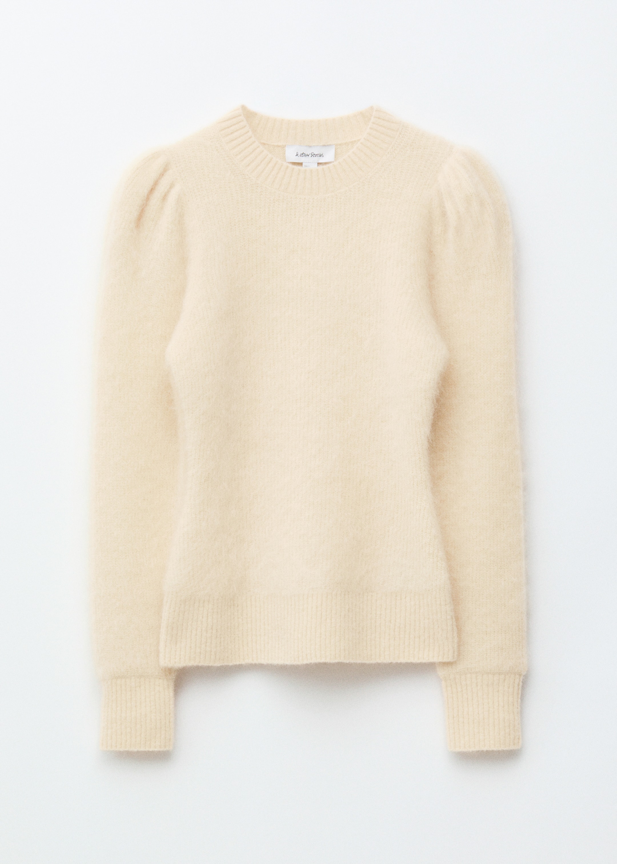 Ver imagem maior: Uma camisola de malha em creme com um acabamento escovado é apresentada como de FRENTE, com mangas compridas bufantes e gola, punhos e bainha canelados, exibindo o seu corte regular.