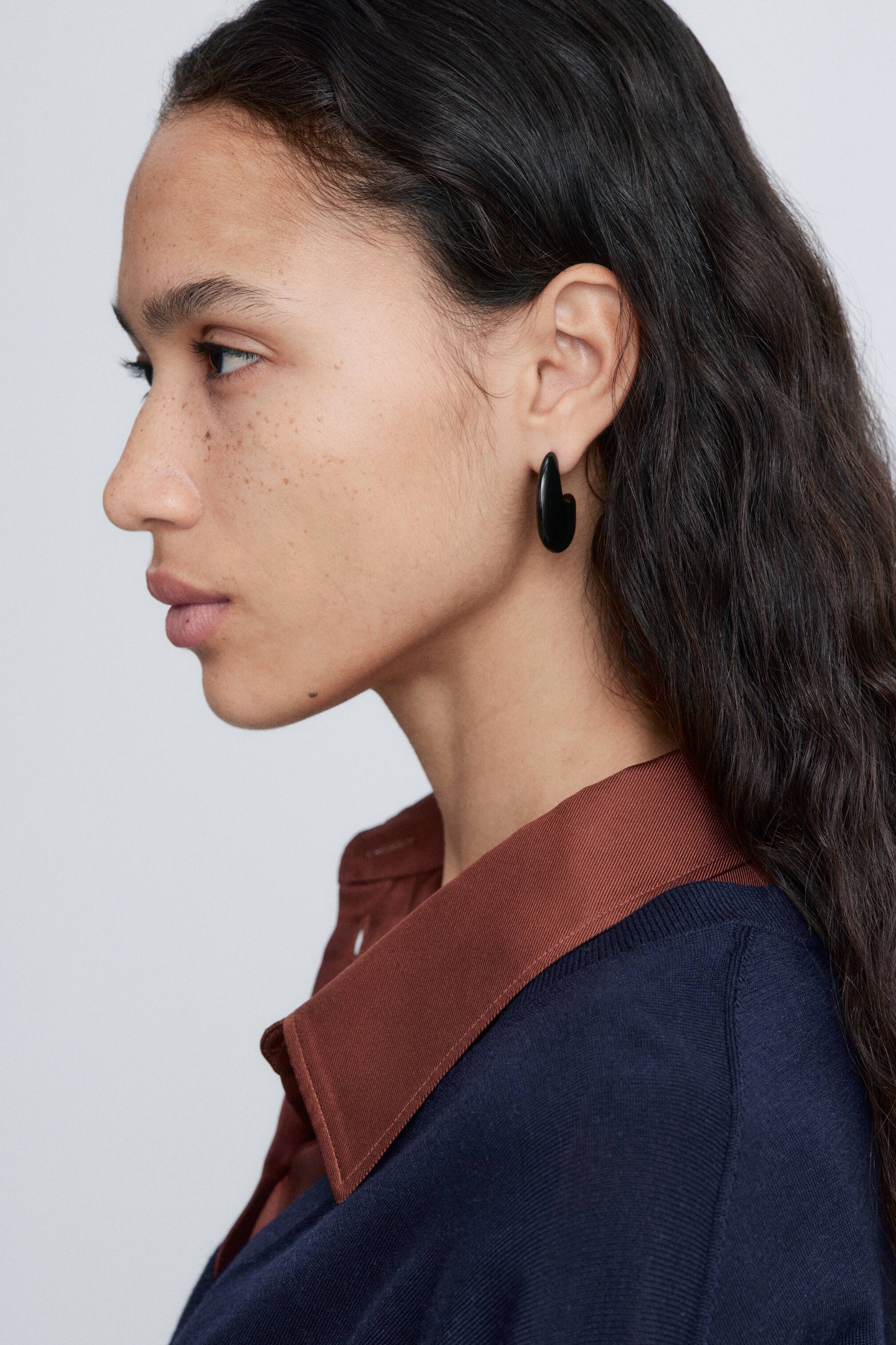 Visa större bild: Svart, klumpiga örhängen med en skulpterad droppform bärs av modellen på hennes örsnibb.