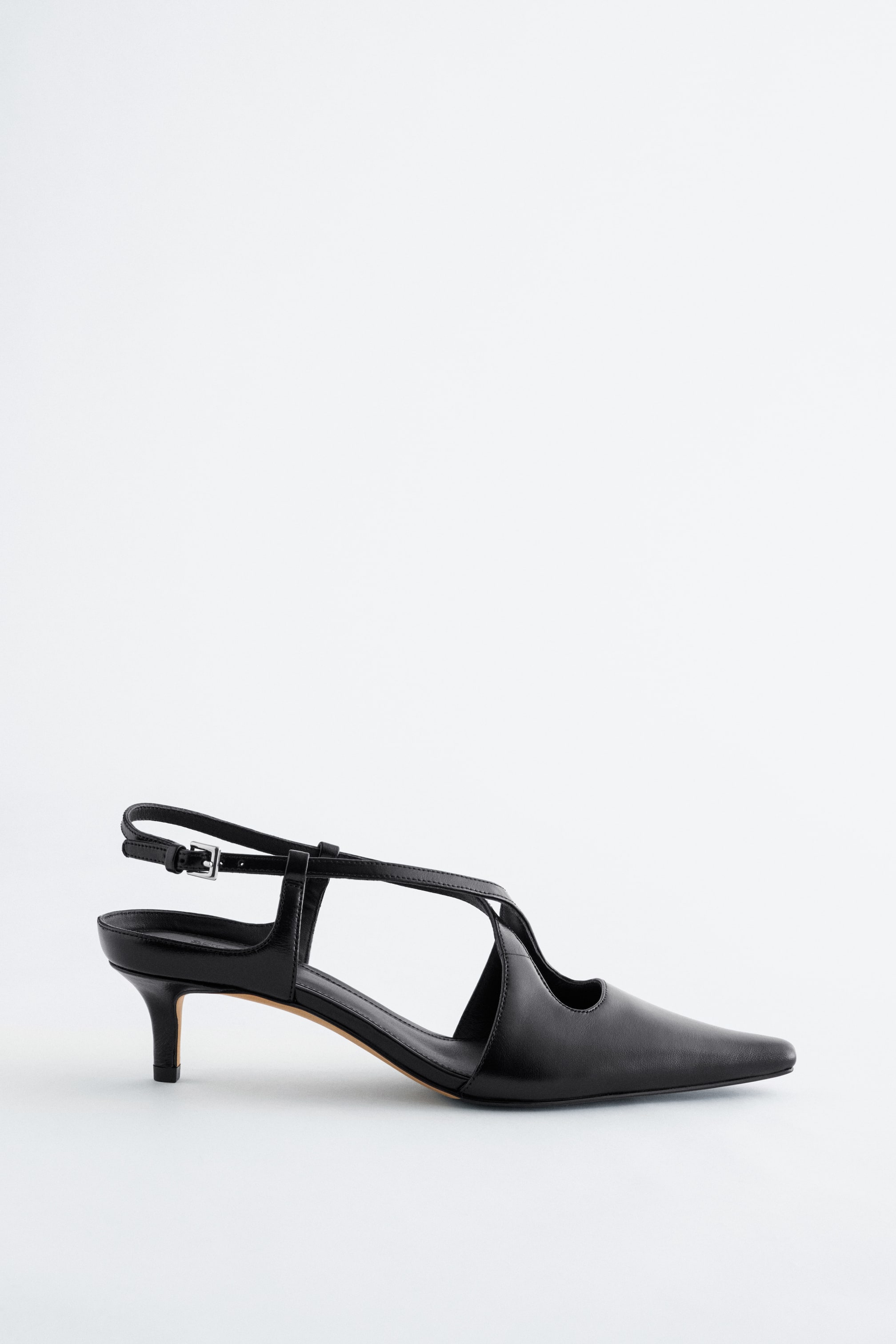 Zobrazit větší obrázek: Černá lodička se špičatou špičkou (slingback) je zobrazena z profilu a má jemný podpadek typu kitten. Je navržena s nastavitelným páskem se sponou v oblasti paty a s dalšími pásky křížícími se přes nárt, které vytvářejí otevřené boční výřezy.