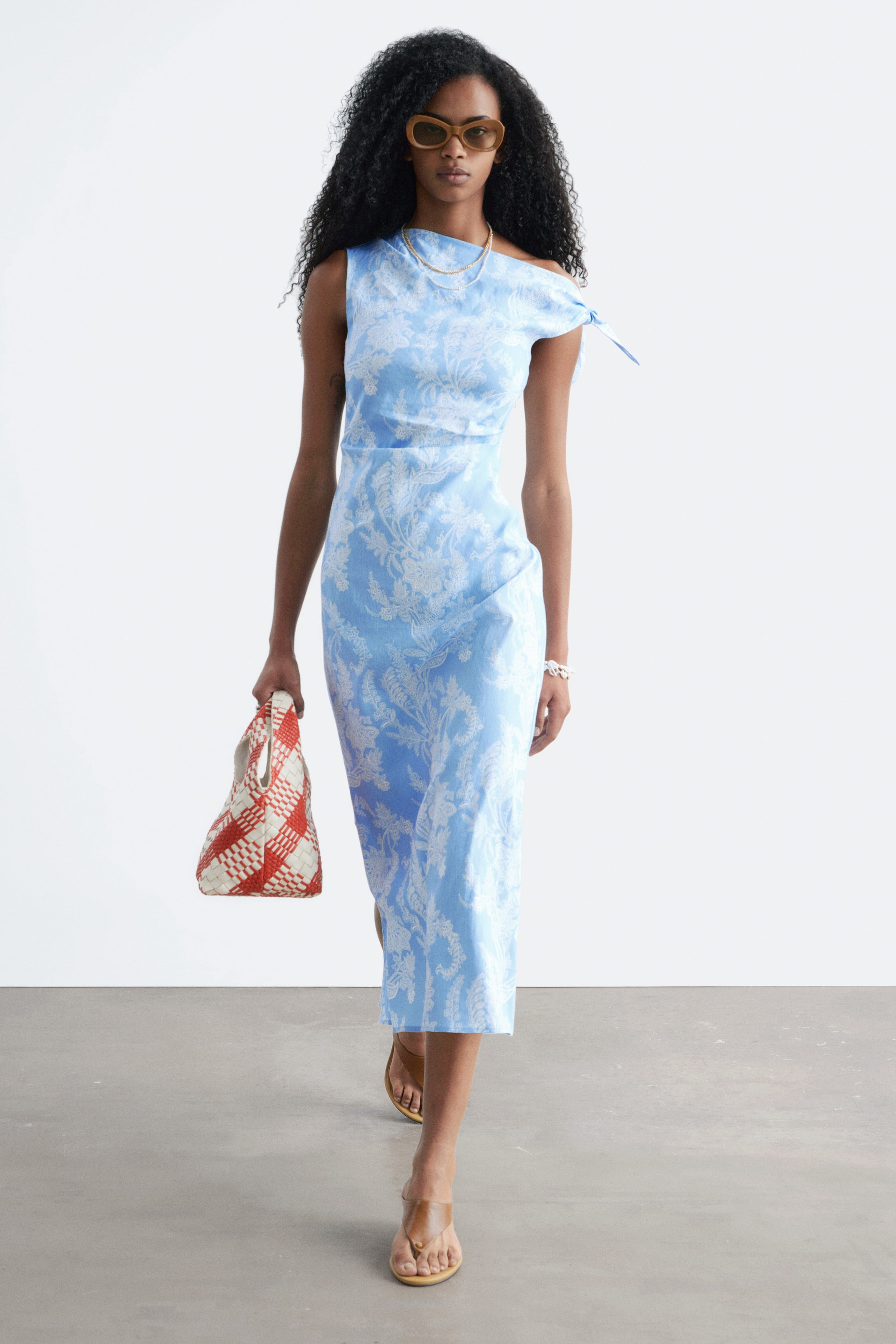 Ver imagen más grande: Un vestido midi azul claro con un estampado floral blanco y un diseño asimétrico de un solo hombro con un detalle de lazo en el hombro derecho.