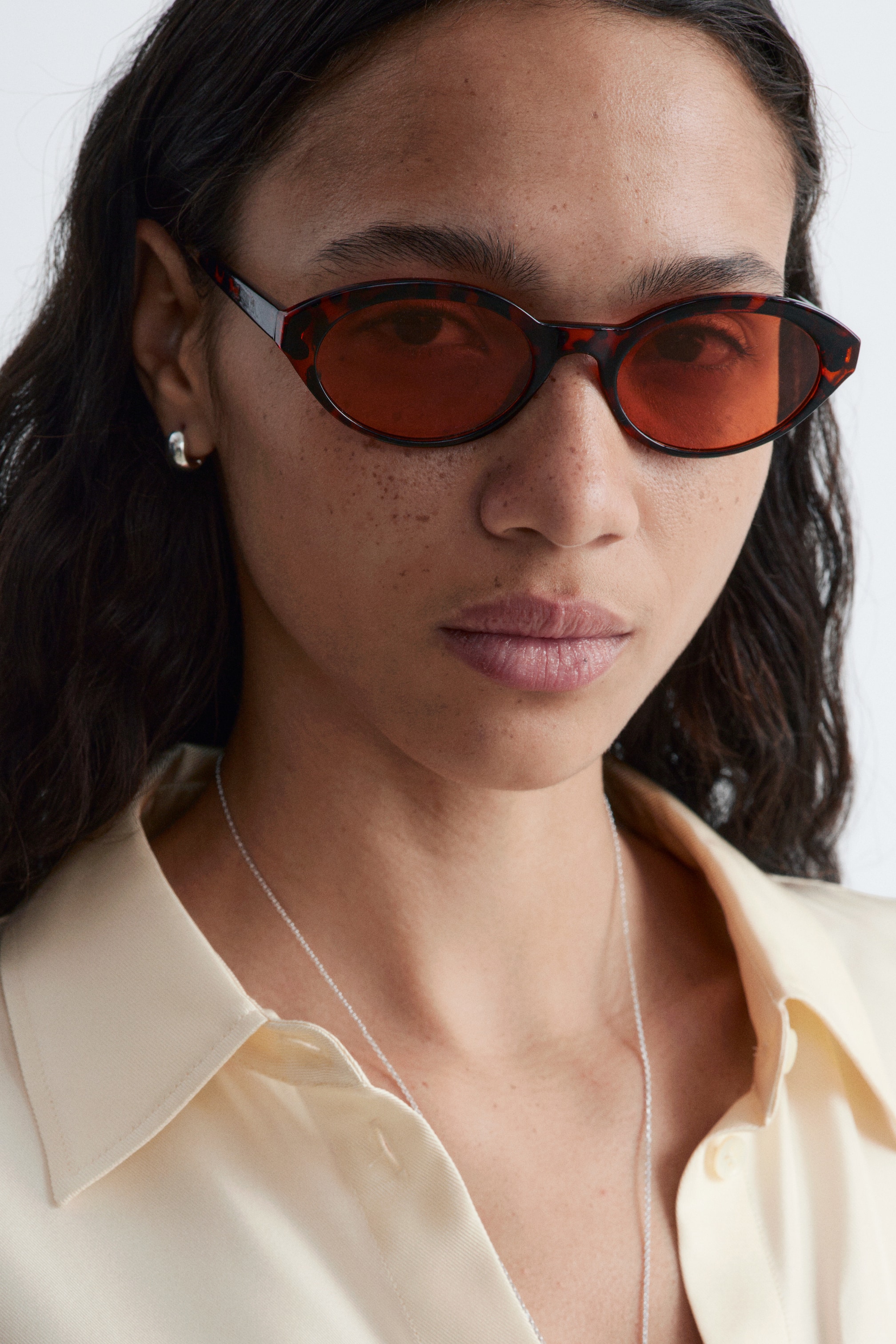 Agrandir l'image: Les lunettes de soleil présentent des montures ovales étroites et allongées avec un motif écaille de tortue, équipées de verres teintés orange. Elles sont portées sur le visage d'une personne, orientées vers l'avant.