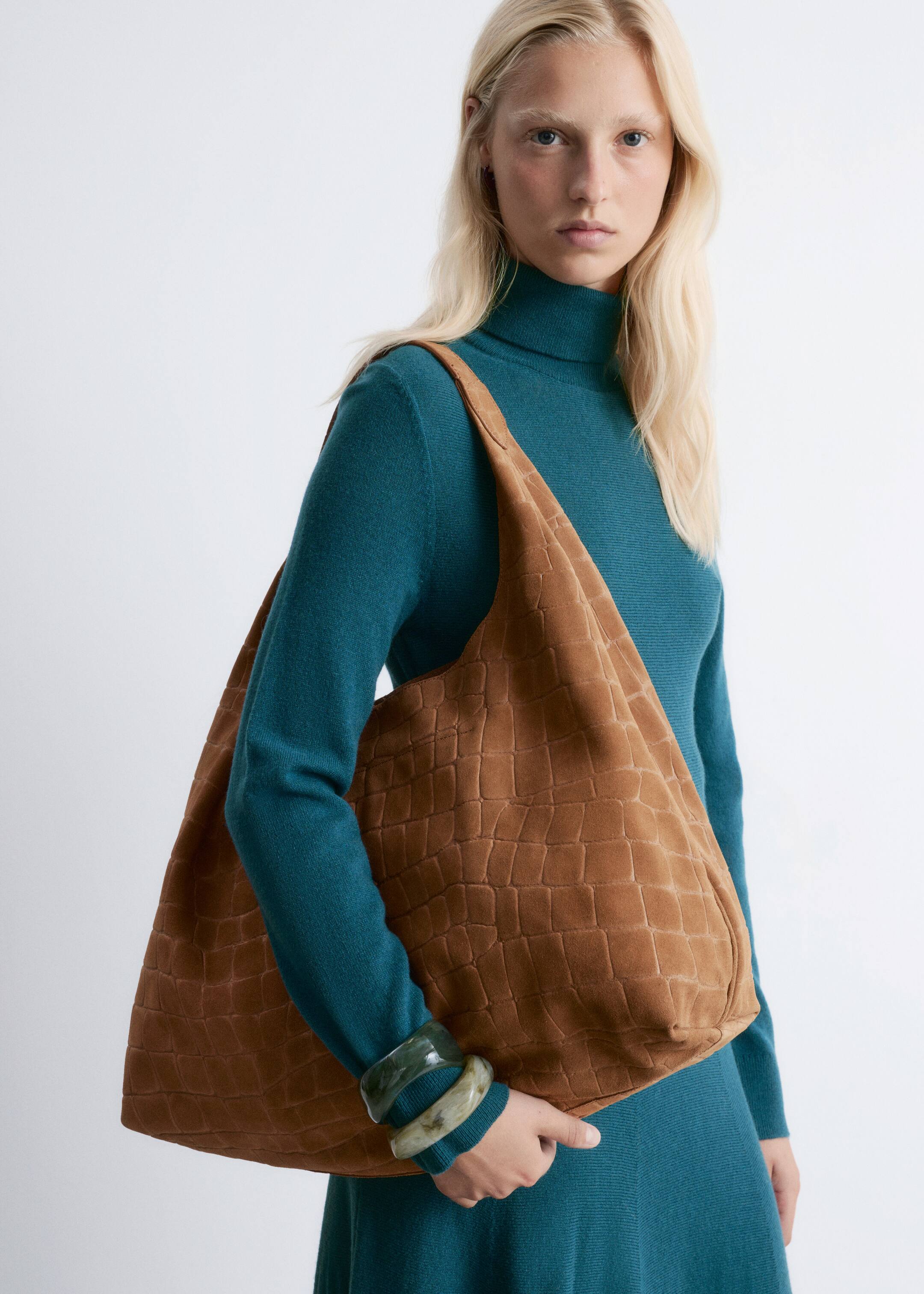Visualizza immagine più grande: Una borsa hobo marrone, realizzata in un materiale simile al camoscio con un motivo a coccodrillo in rilievo, è indossata sulla spalla, con il corpo principale rivolto in avanti.