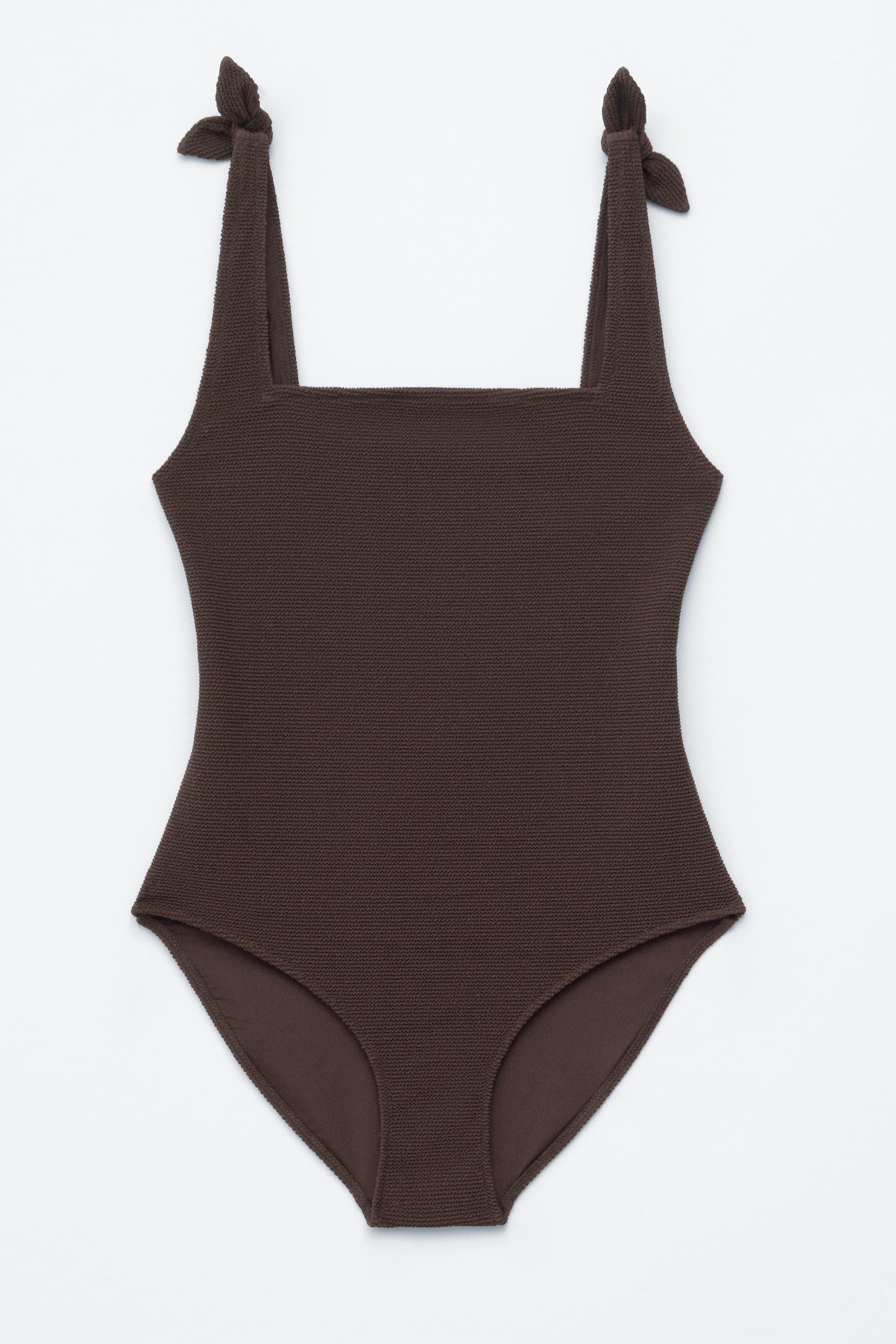 Ver imagen más grande: Se presenta DE FRENTE un bañador de una pieza texturizado en marrón, con escote cuadrado y lazos decorativos en los hombros.