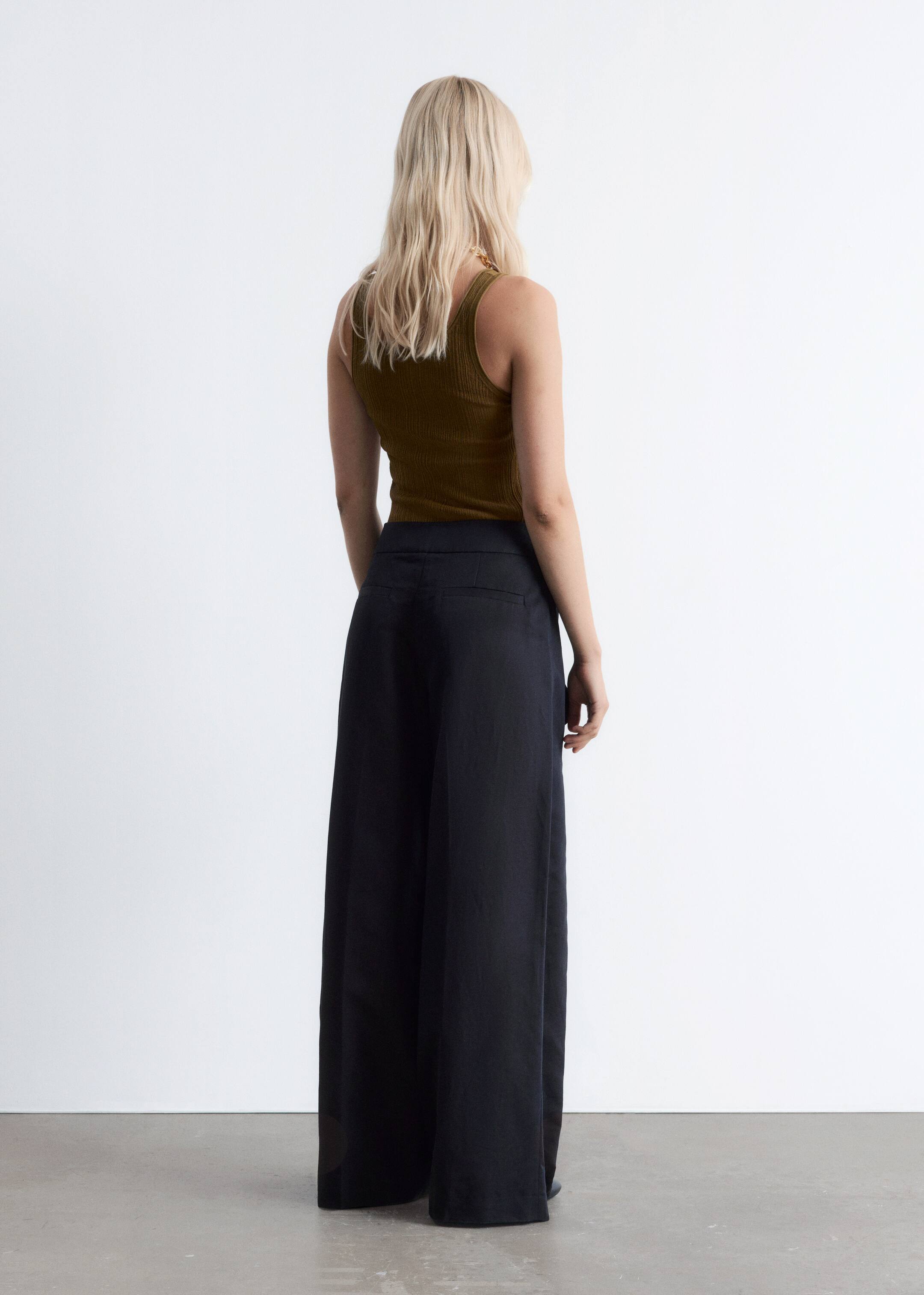 Grotere afbeelding bekijken: Een olijfgroen geribd tanktop wordt gedragen, ingestopt in een donkere, hoog getailleerde, wijde broek, waarbij beide kledingstukken van achteren worden bekeken.