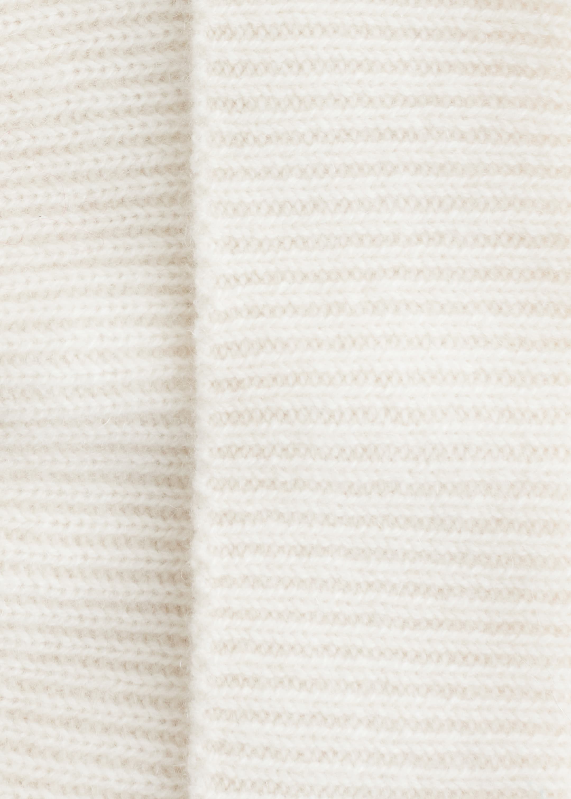 Größeres Bild anzeigen: Eine cremefarbene Mütze wird in einer Nahaufnahme gezeigt, die ihre gerippte Strickstruktur zeigt. Eine markante vertikale Falte definiert ihren umgeschlagenen Rand.