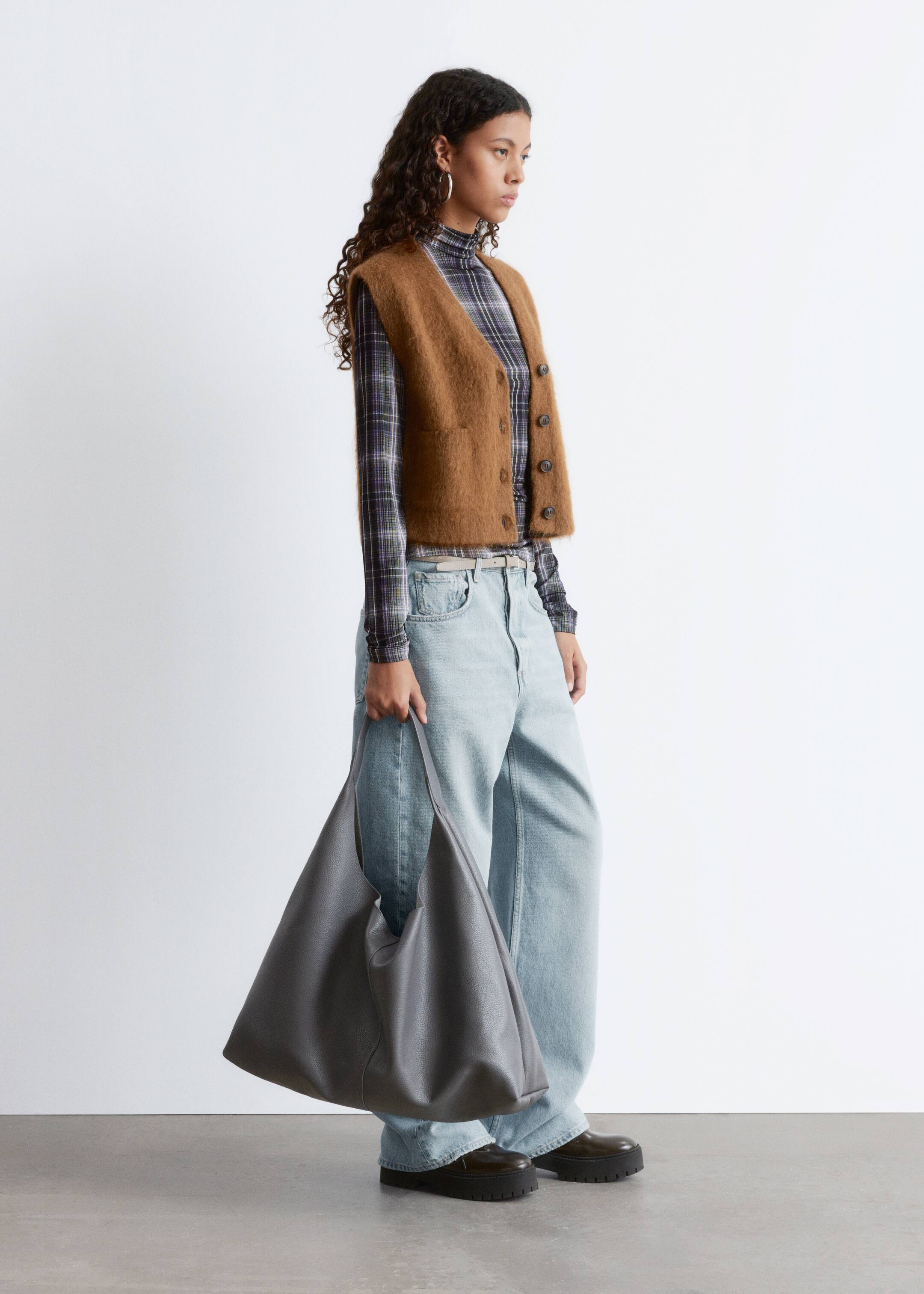 Visa större bild: En stor, grå hobo-väska med en texturerad yta hålls i dess enda rem, vilket visar upp dess mjuka, ostrukturerade form från en framsida vy.