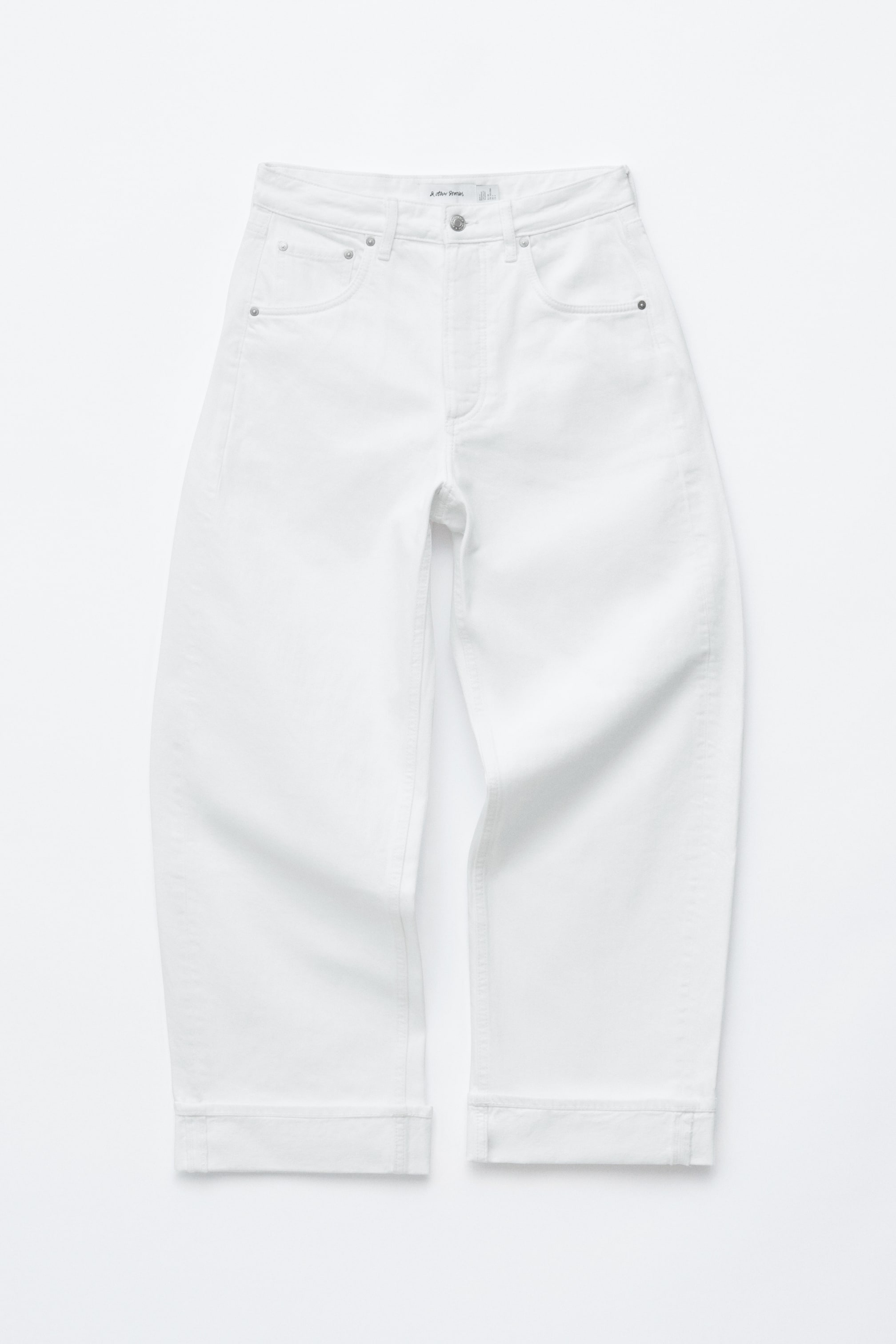 Visa större bild: Vita jeans presenteras av FRONT, med en klassisk 5-ficksdesign, en medelhög midja och knäppgylf. Den oversized passformen visar upp tunnformade, extra långa ben, båda stylade med uppvikta muddar vid fållen.