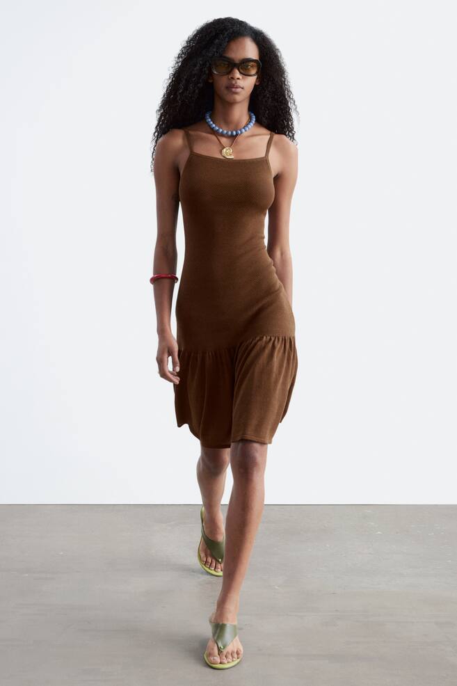 The brown ribbed knit mini dress features thin spaghetti straps and a close-fitting bodice. The dress flares into a ruffled tier at the hem, presented facing forward. - 1