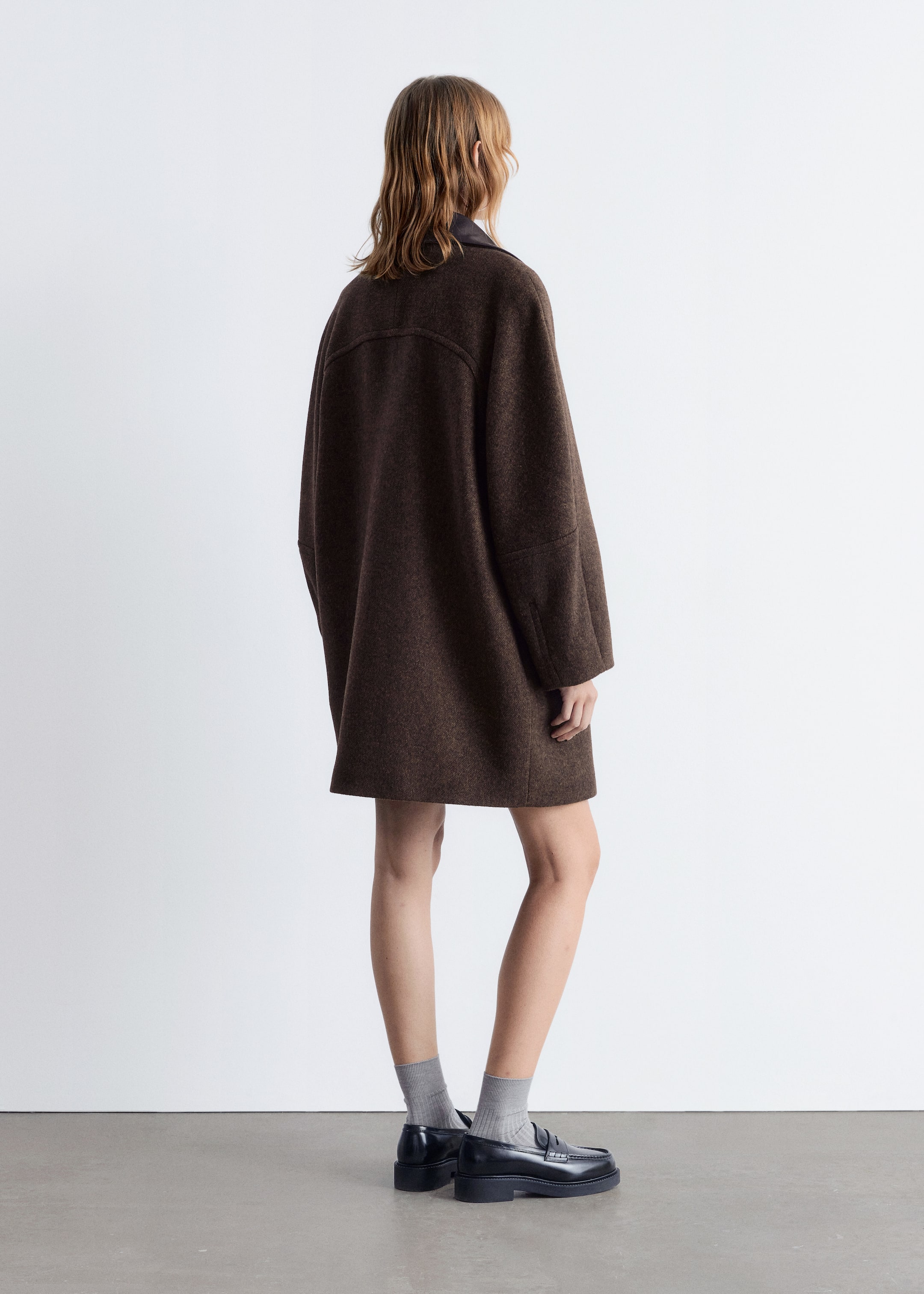View larger image: A brown, textured oversized coat is being presented from the back, featuring dropped shoulders and wide, straight sleeves. A distinct horizontal yoke seam is visible across the upper back, and a dark collar is showing at the neckline.
