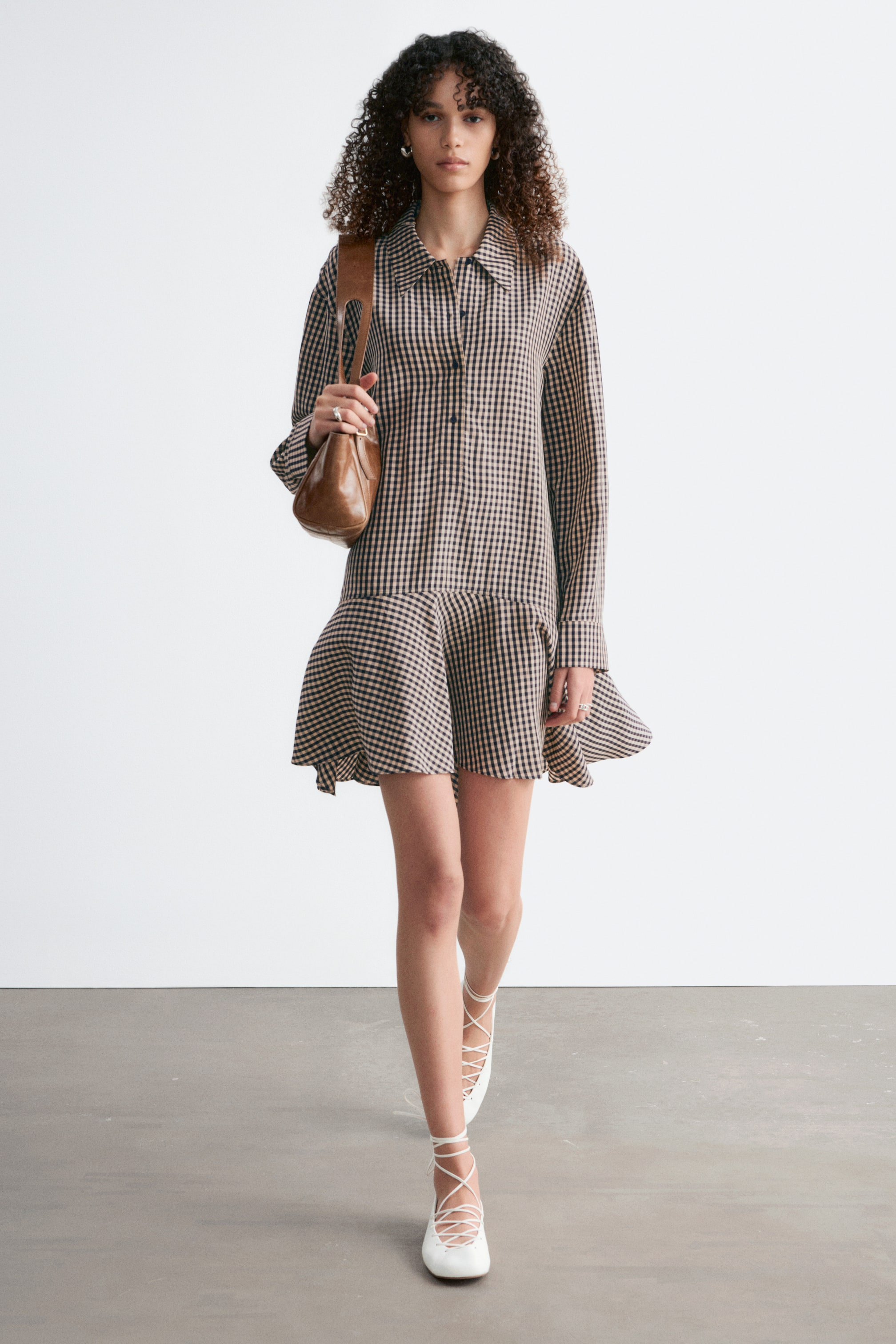 Vis større bilde: En brun og beige rutete skjortekjole har en spiss krage, en knappet front og lange ermer med knappede mansjetter. Den har en løs passform med et lagdelt, rynket kant som faller over kneet.