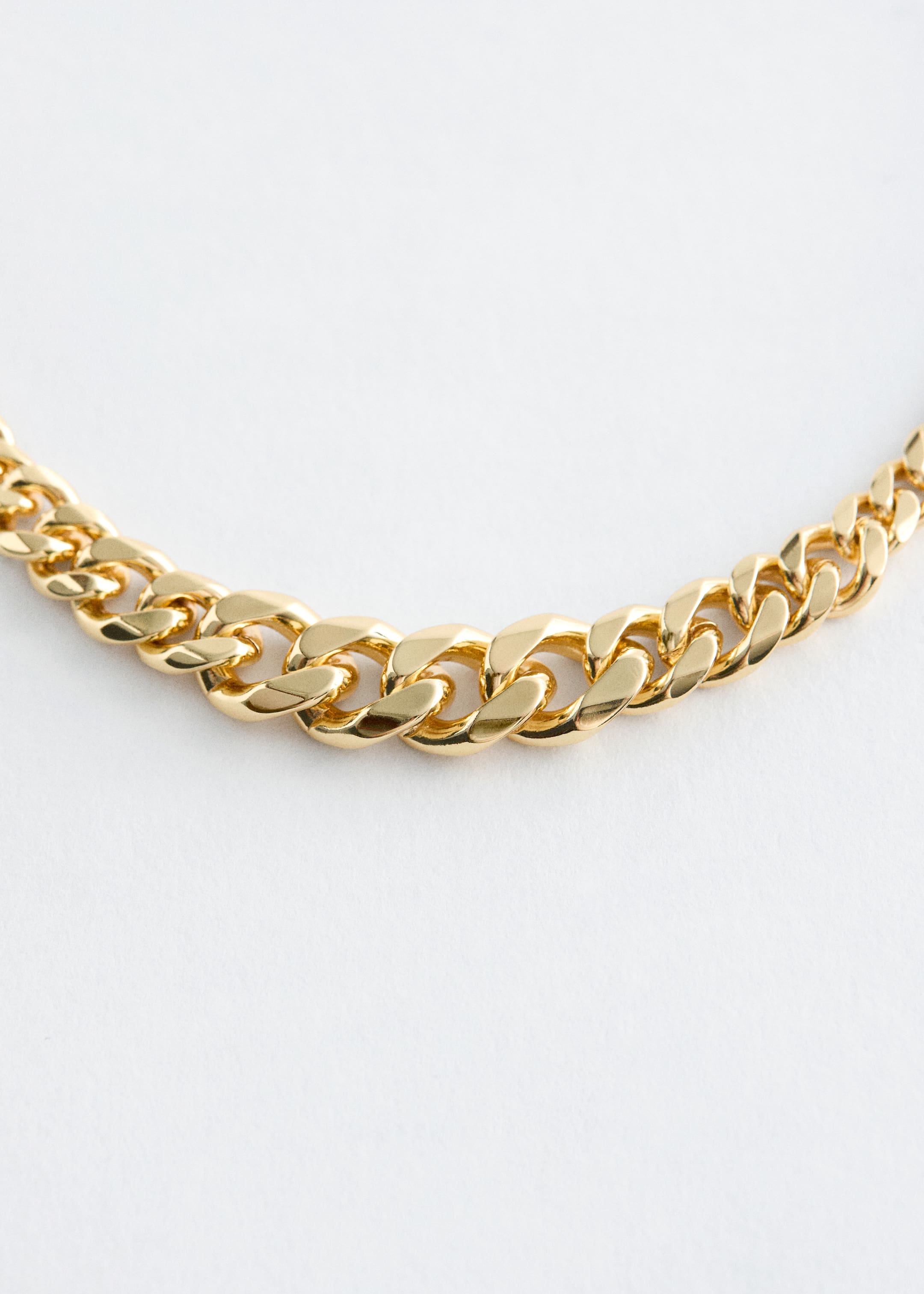 Ingrandisci l'immagine: Una collana a catena lucida con tonalità dorata è distesa piatta, caratterizzata da maglie curb simmetriche che diventano visibilmente più spesse verso il centro.