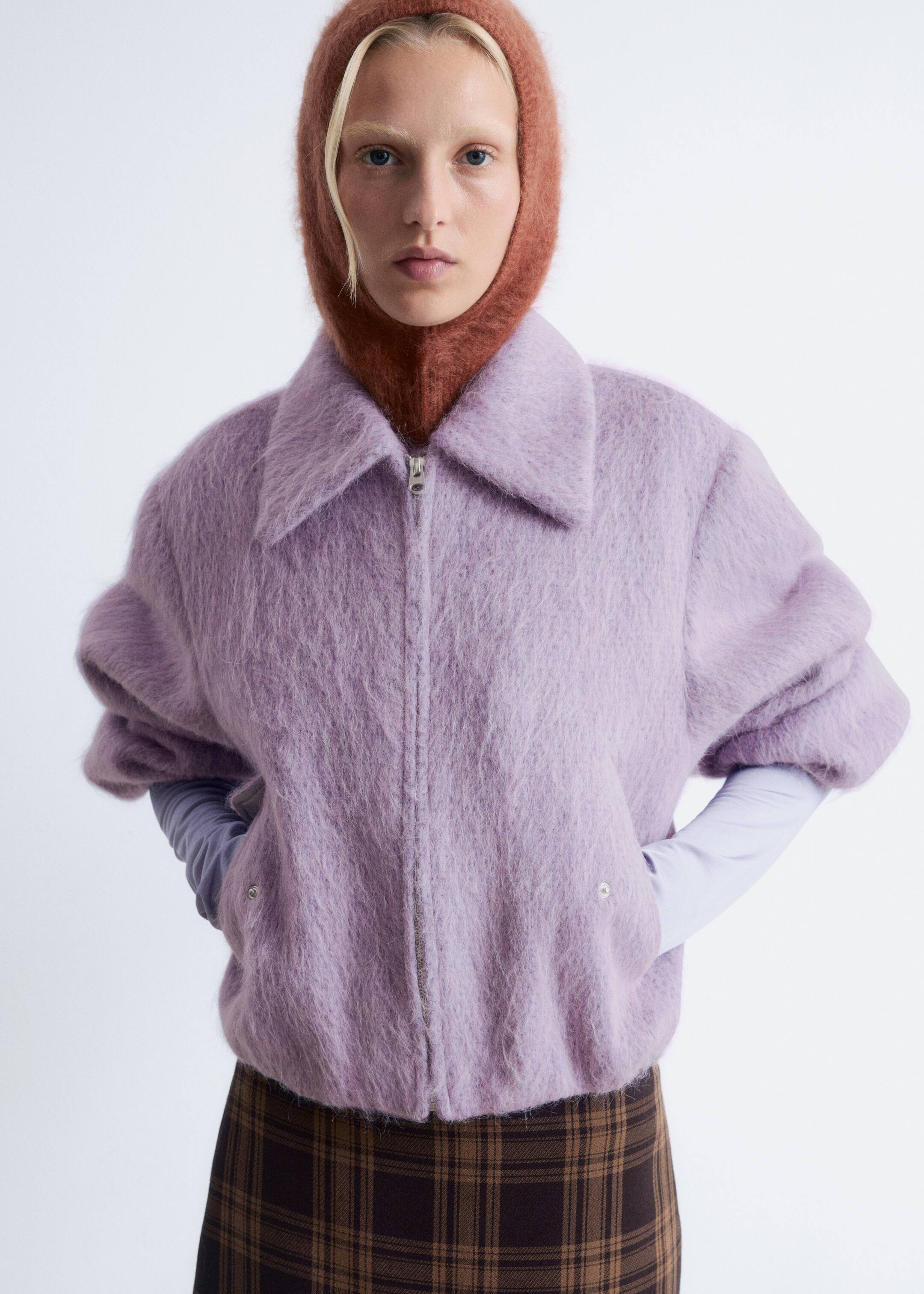 Agrandir l'image: Une veste lilas duveteuse est orientée vers l'avant, présentant un large col évasé et une fermeture éclair frontale de ton argenté. Elle présente des manches courtes volumineuses superposées à un haut à manches longues de couleur claire, et est finie avec un ourlet élastiqué.