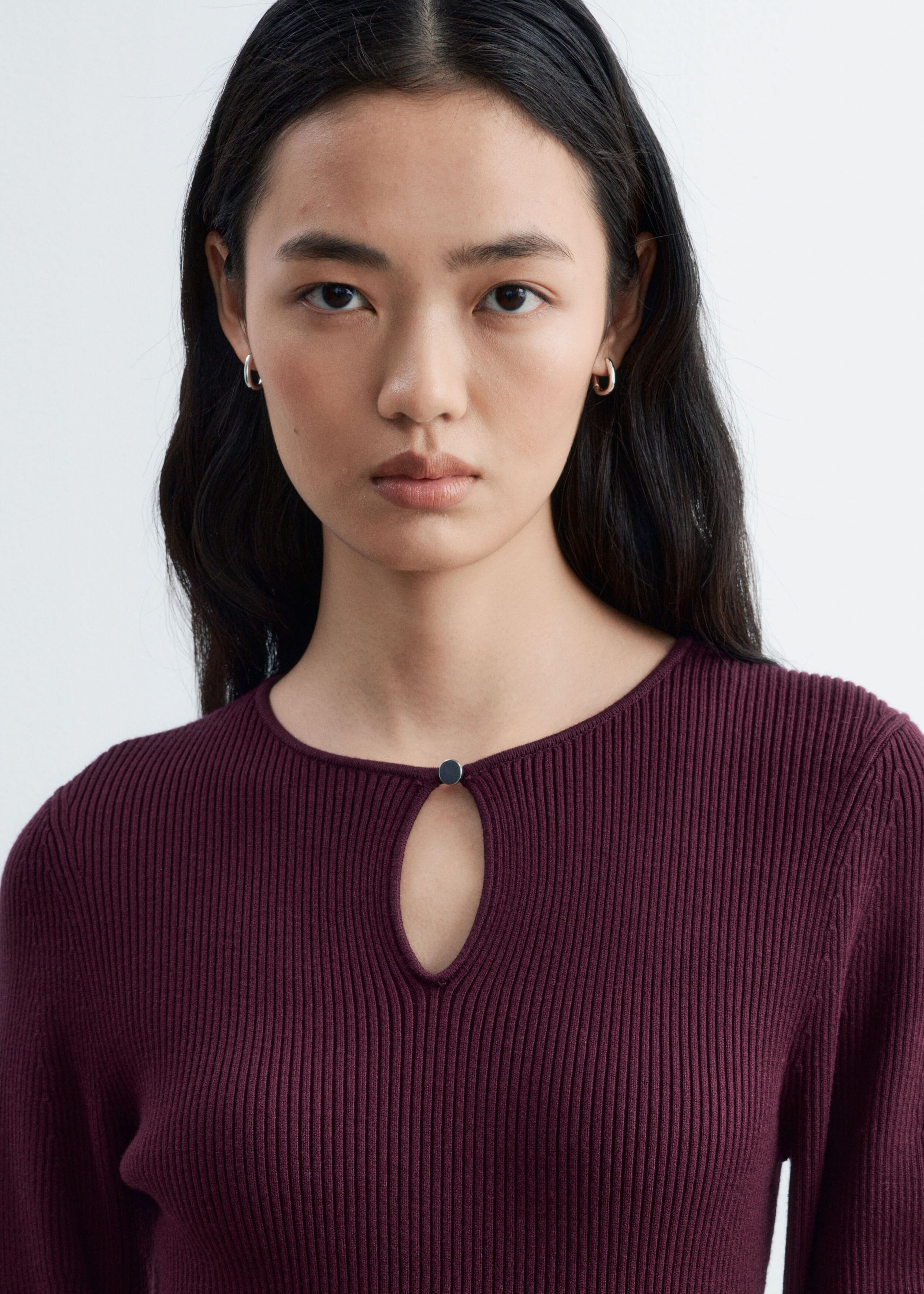 A ribbed knit burgundy dress featuring a keyhole opening with a small metal button at the crew neckline is being worn by the model. The close-up view highlights the vertical ribbed texture of the fabric.