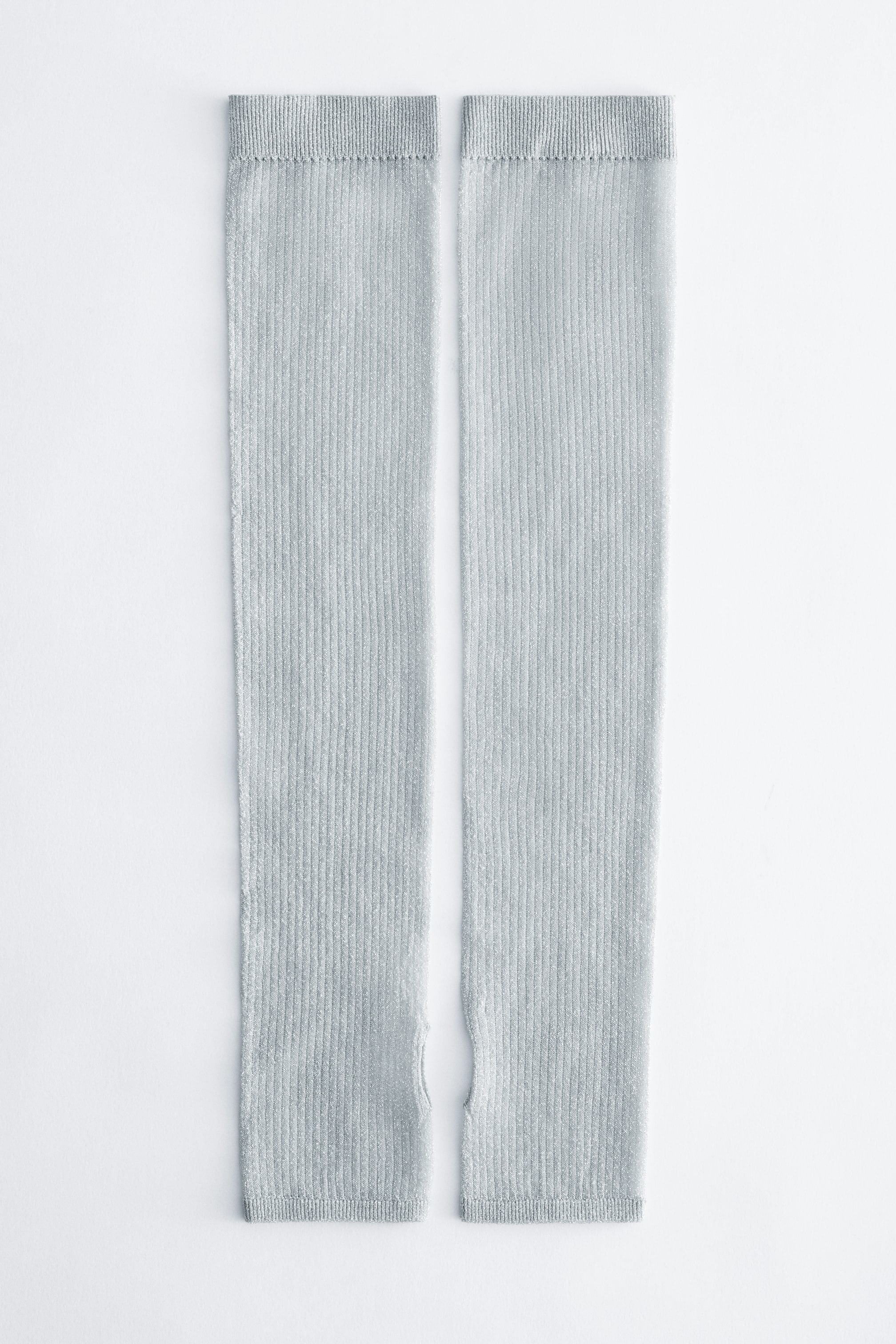 View larger image: A pair of light grey, ribbed-knit arm warmers lies flat, showing the front design. The arm warmers feature a vertical ribbed texture throughout, elasticised top bands, and integrated thumbholes near the bottom cuffs.