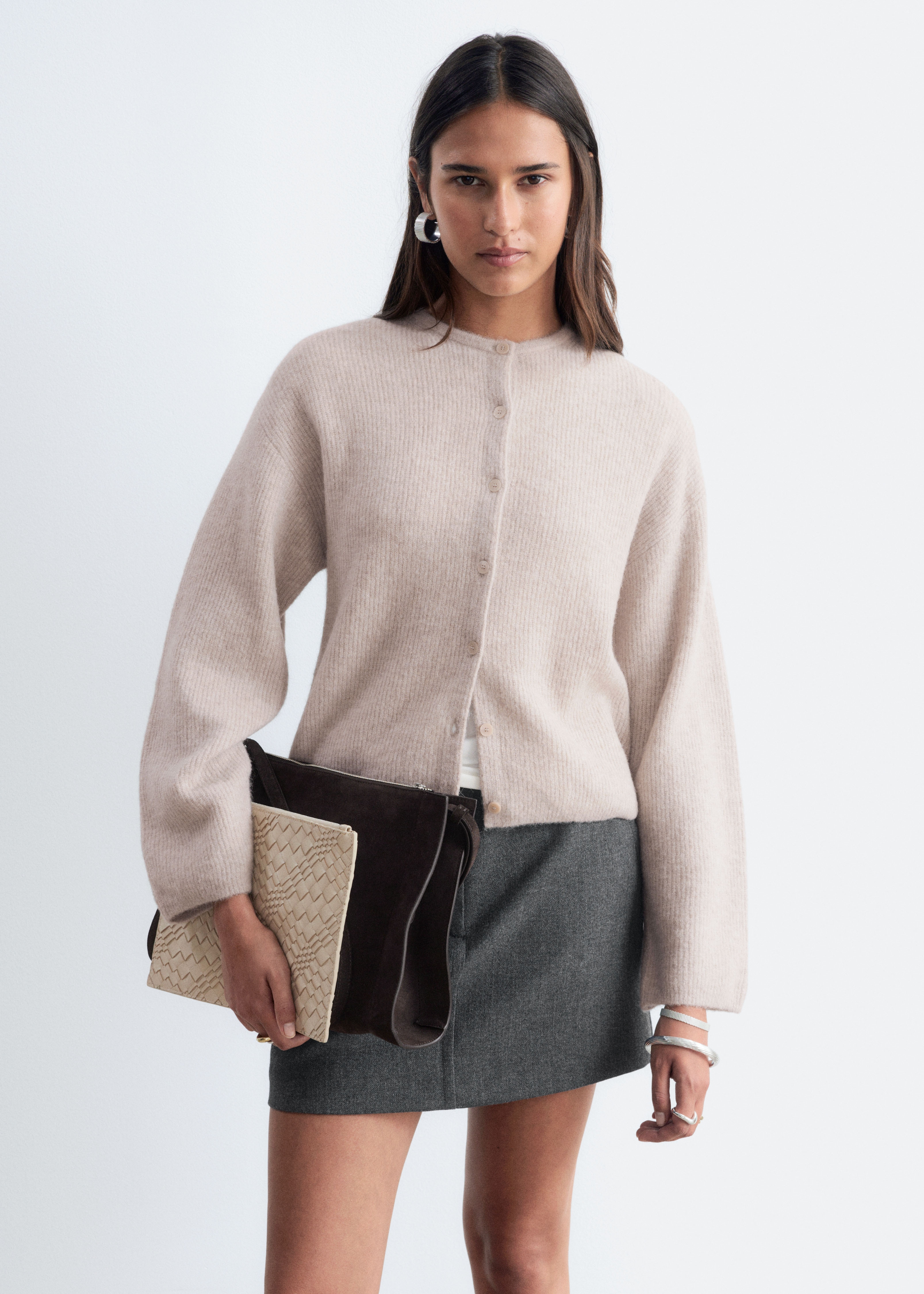 Un cardigan a maniche lunghe è presentato in vista frontale, mostrando la sua trama lavorata a maglia beige, morbida e leggermente pelosa. Presenta uno scollo rotondo e un'abbottonatura centrale con sei bottoni coordinati.