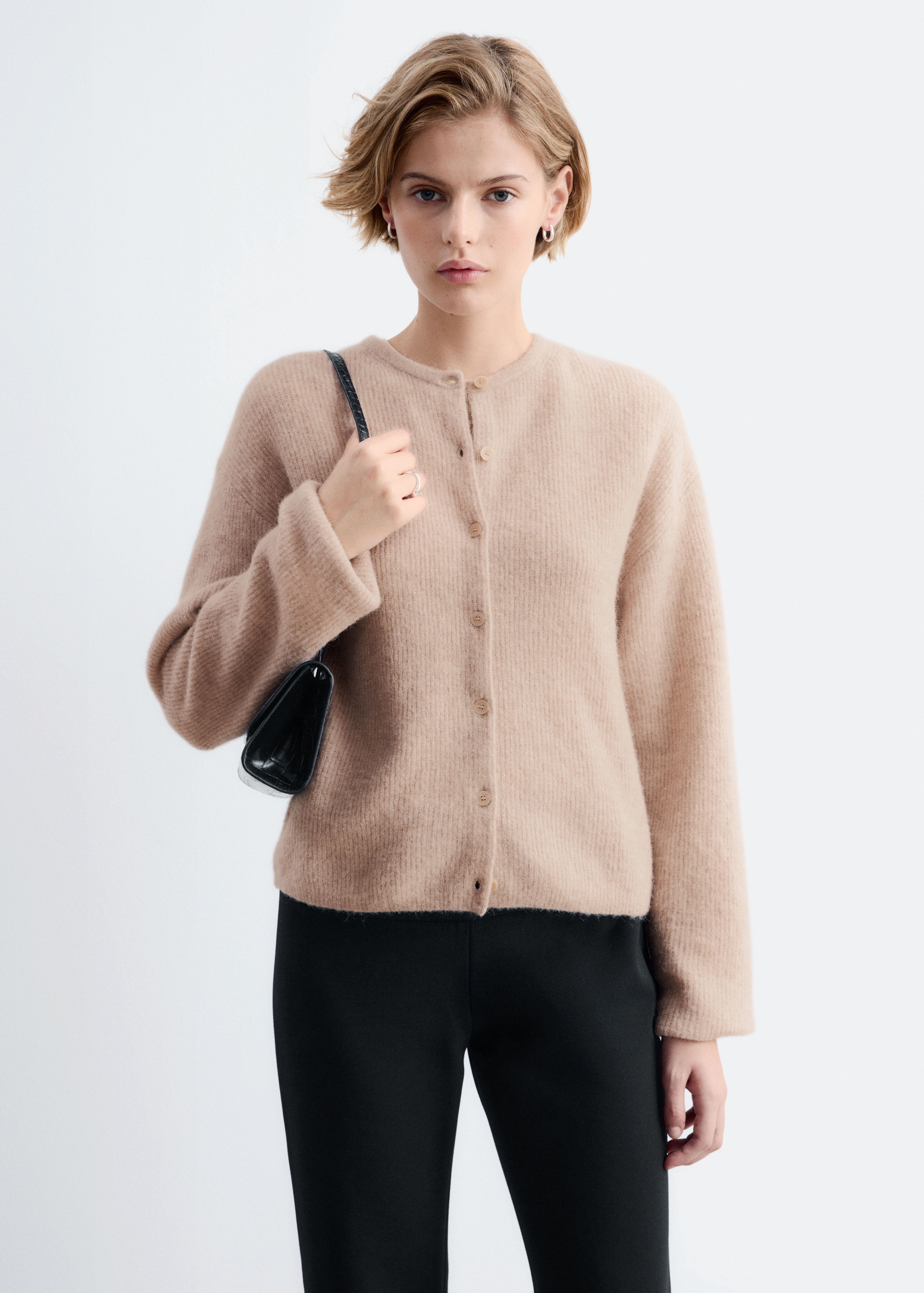 Ein hellbrauner Cardigan wird von vorne präsentiert, mit einem Rundhalsausschnitt und langen Ärmeln. Sechs helle Knöpfe verschließen die Vorderseite in der Mitte, und das Strickmaterial zeigt eine weiche, leicht flauschige Textur.